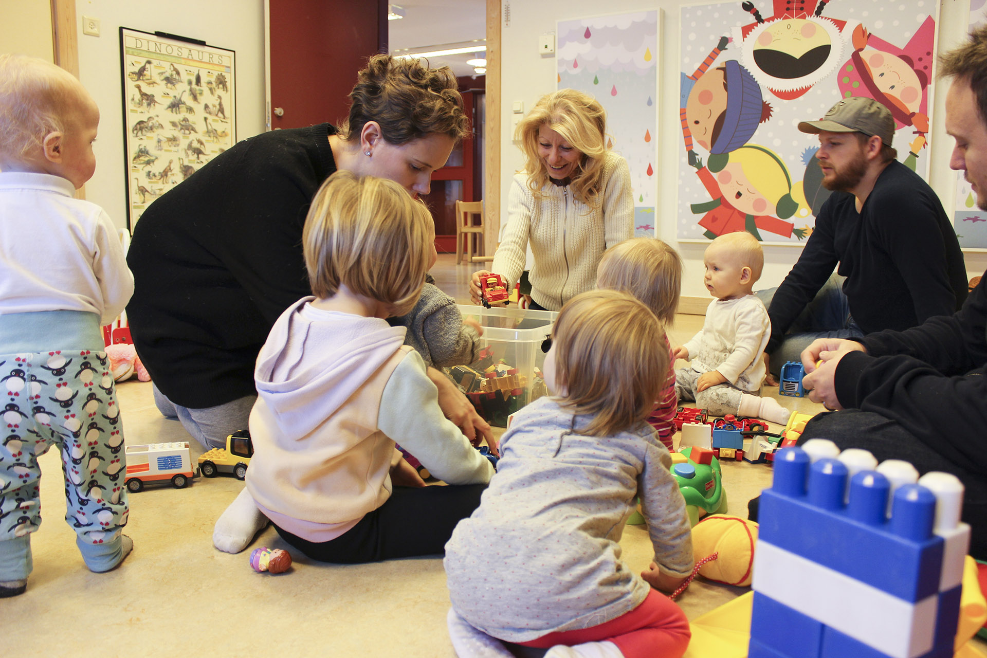 Barn och vuxna leker tillsammans på golvet med bilar och klossar.