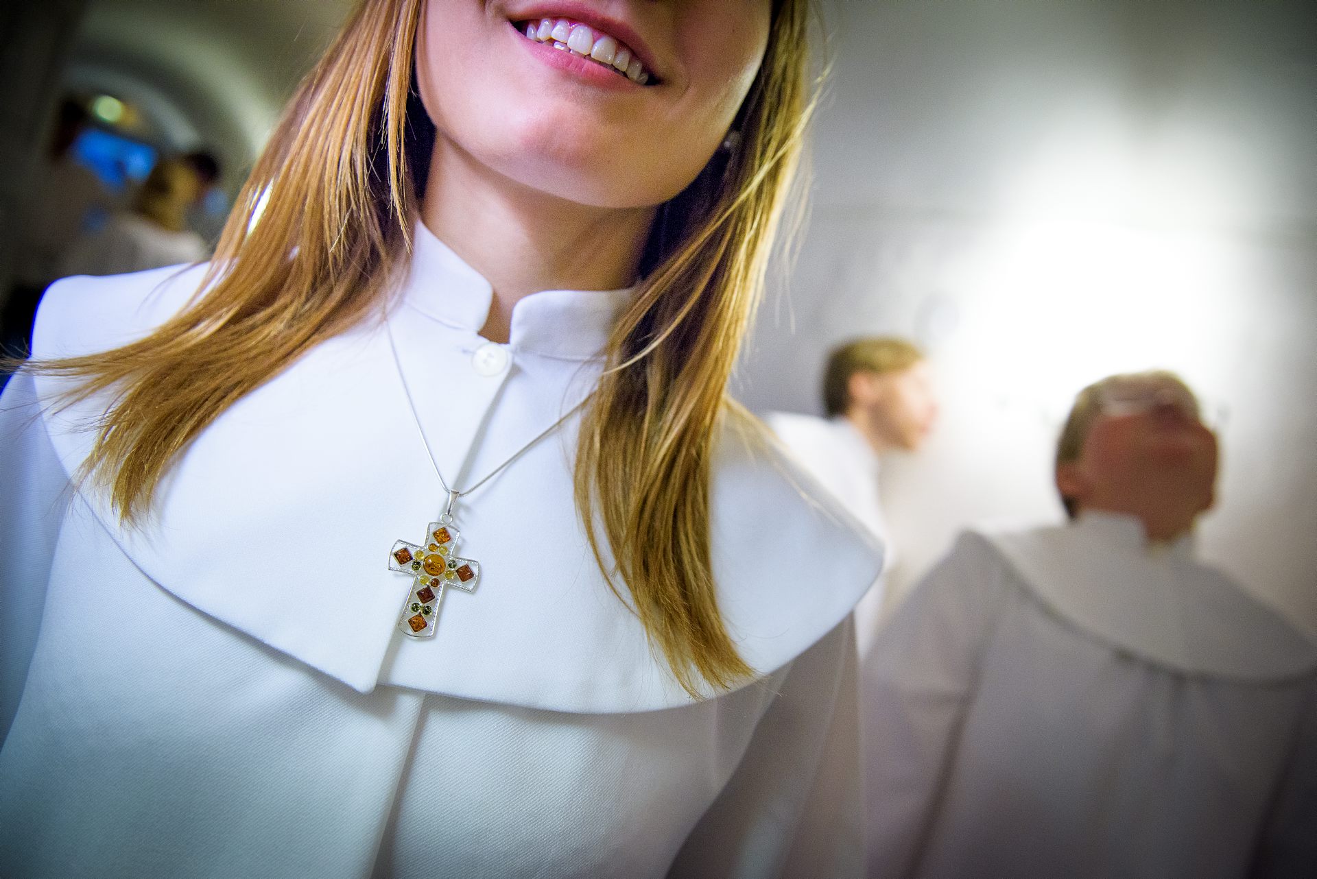 En konfirmand i kåpa och med ett kors i ett halssmycke om halsen.