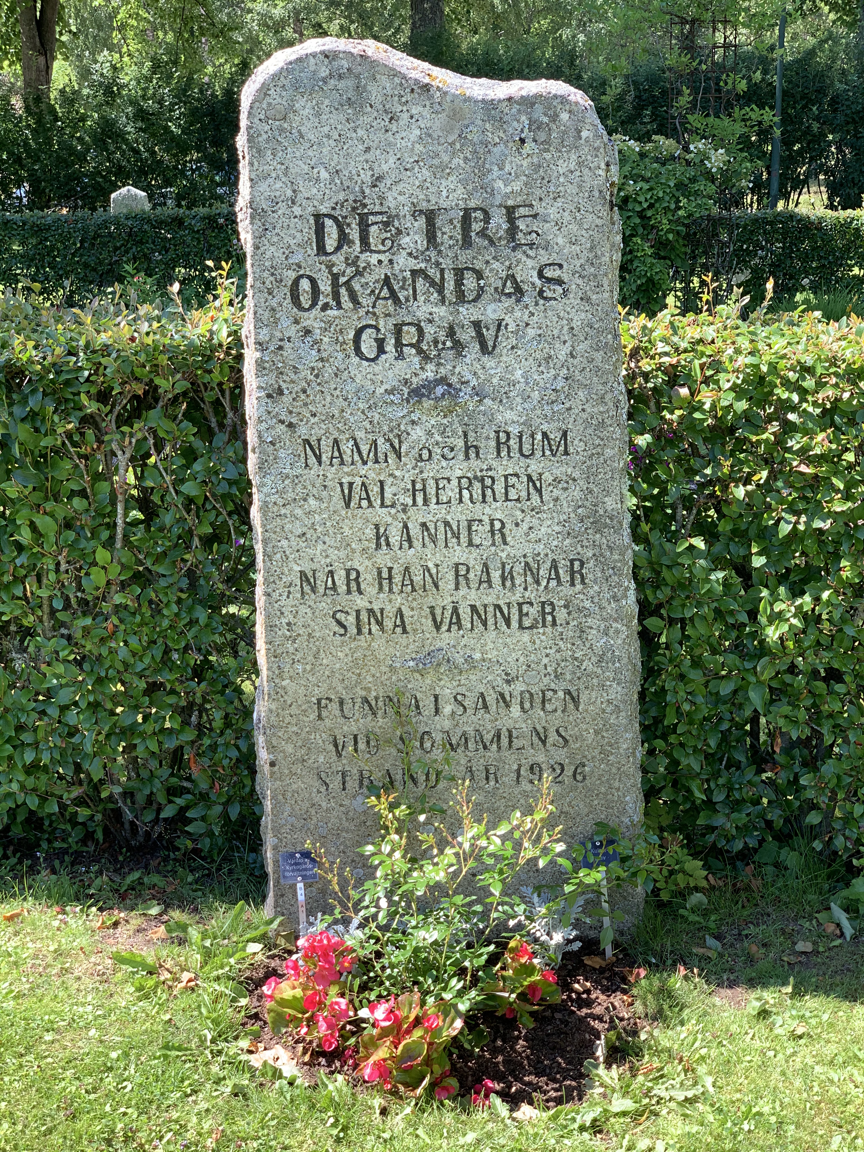 Gravsten på Malexanders kyrkogård med blomsterplantering framför.