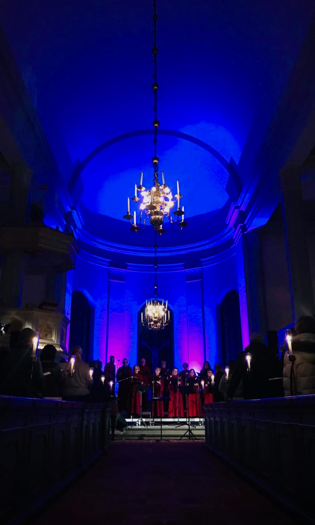En blått upplyst kyrka med ett publikhav i förgrunden av en körkonsert.