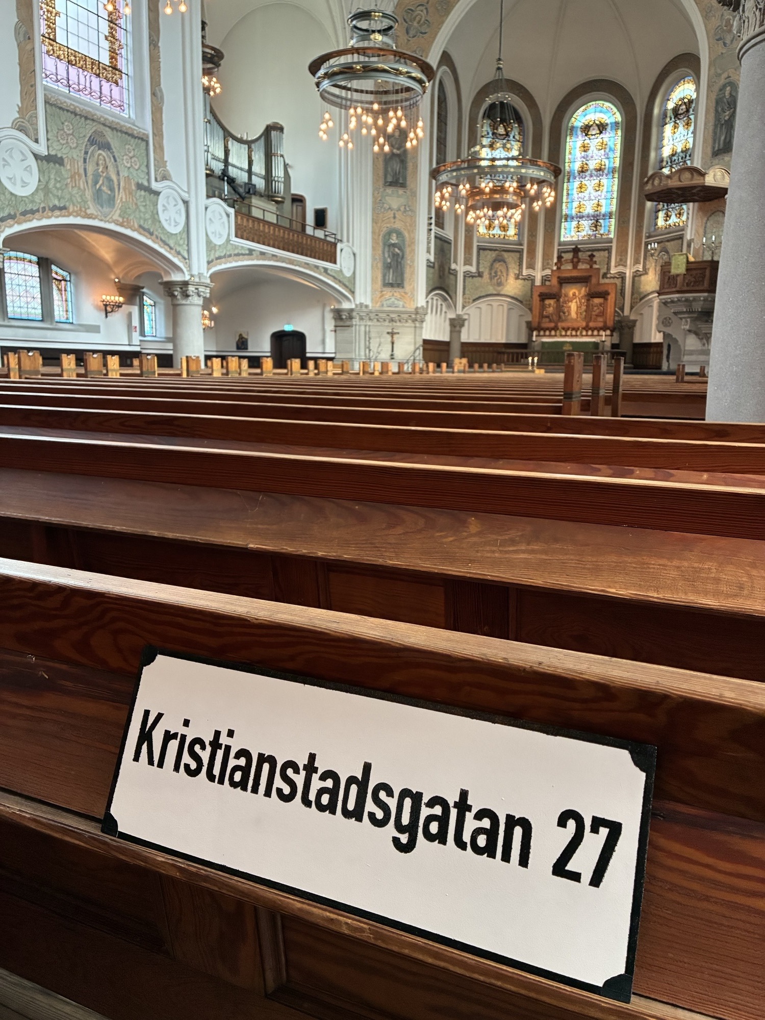 Gatunamnsskylt med Kristianstadsgatan 27 ligger i en kyrkbänk av trä. I bakgrunden skymtas fler bänkar och altaret.