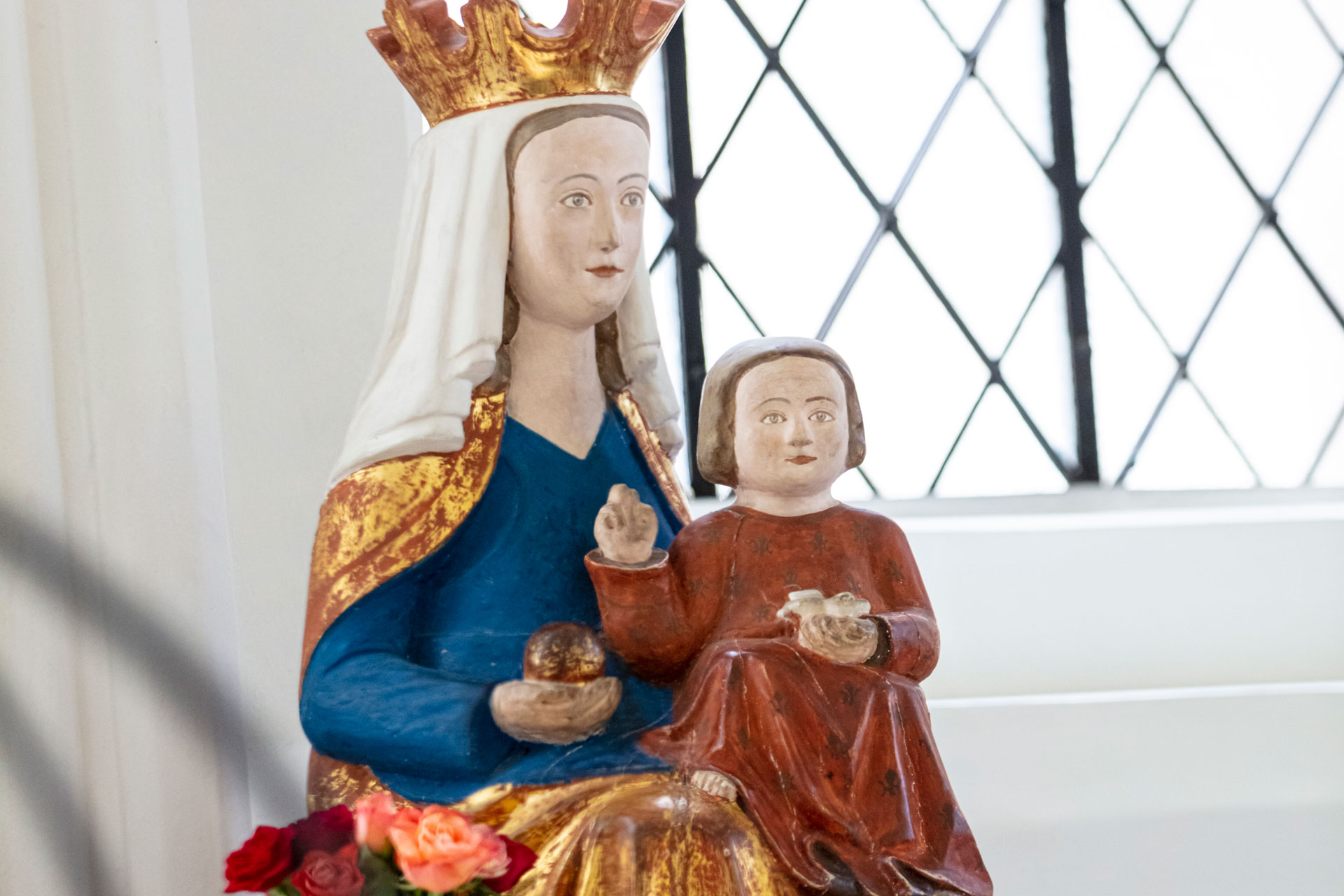 Staty som föreställer en ung kvinna med guldkrona, vitt dok, blå dräkt och gyllene caipe med ett gossebarn i famnen.