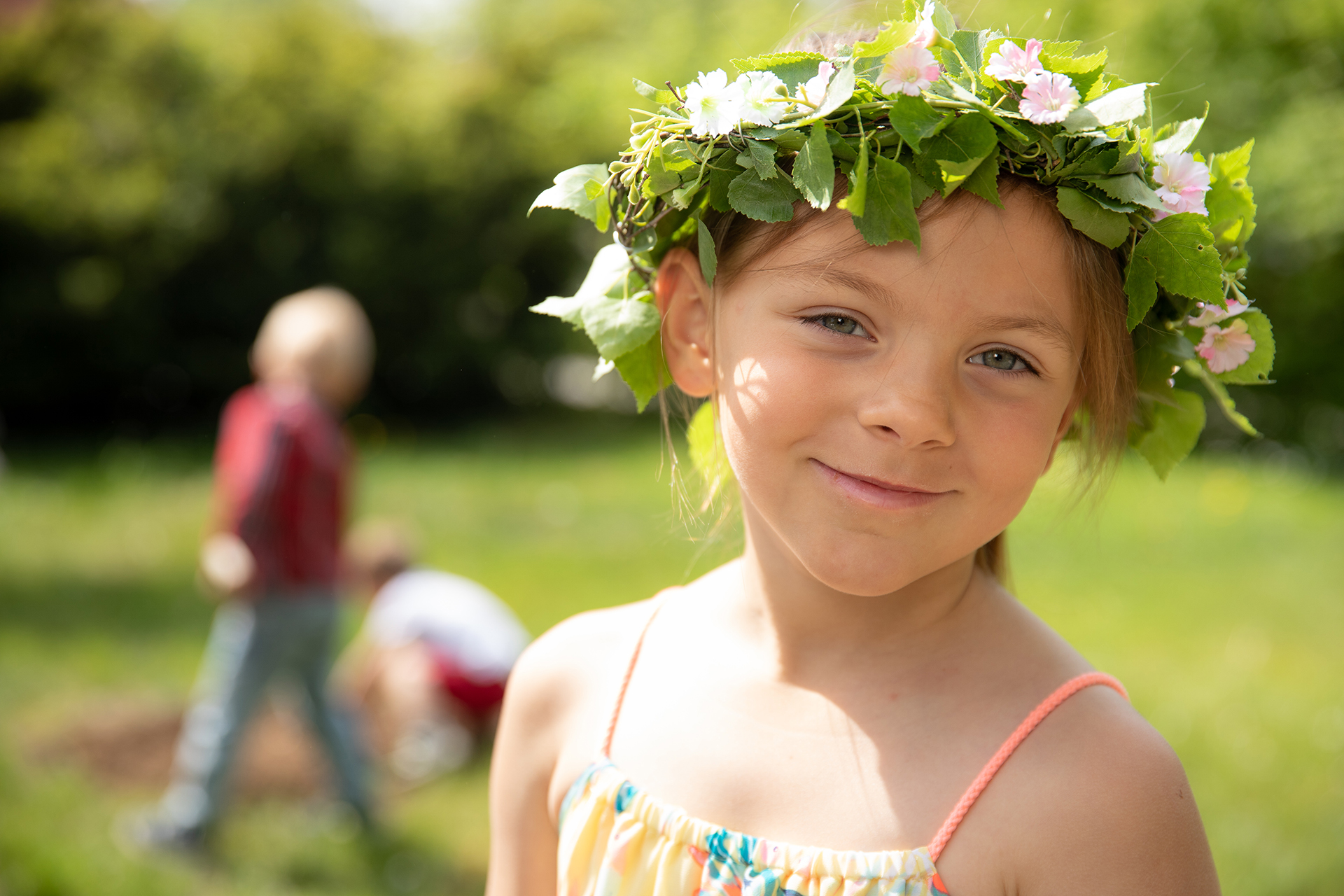 Flicka med blomsterkrans i håret, suddig bakgrund med gräs och människor