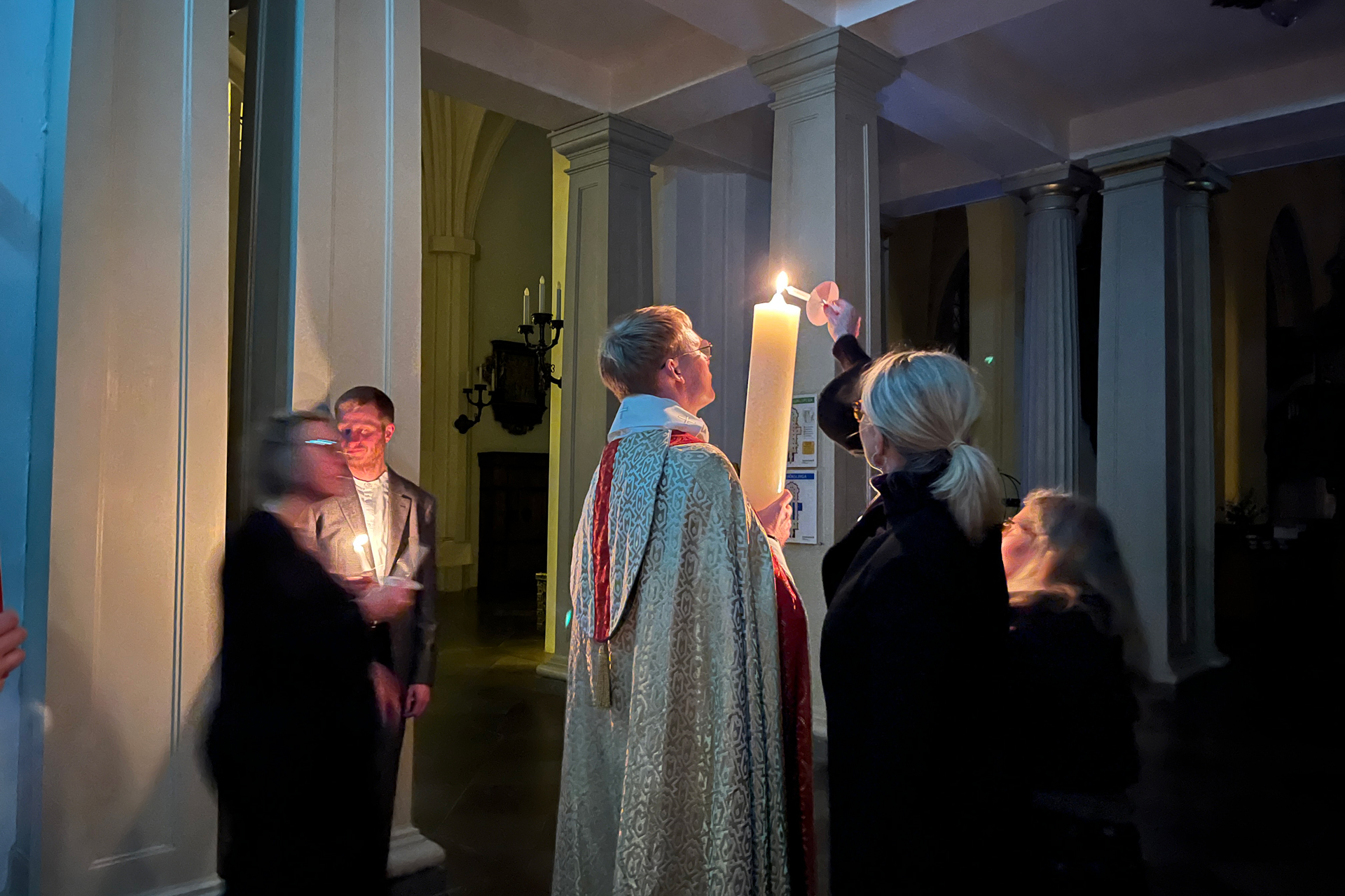 En grupp människor och en präst samlade kring påskljuset som lyfts upp och tänds.