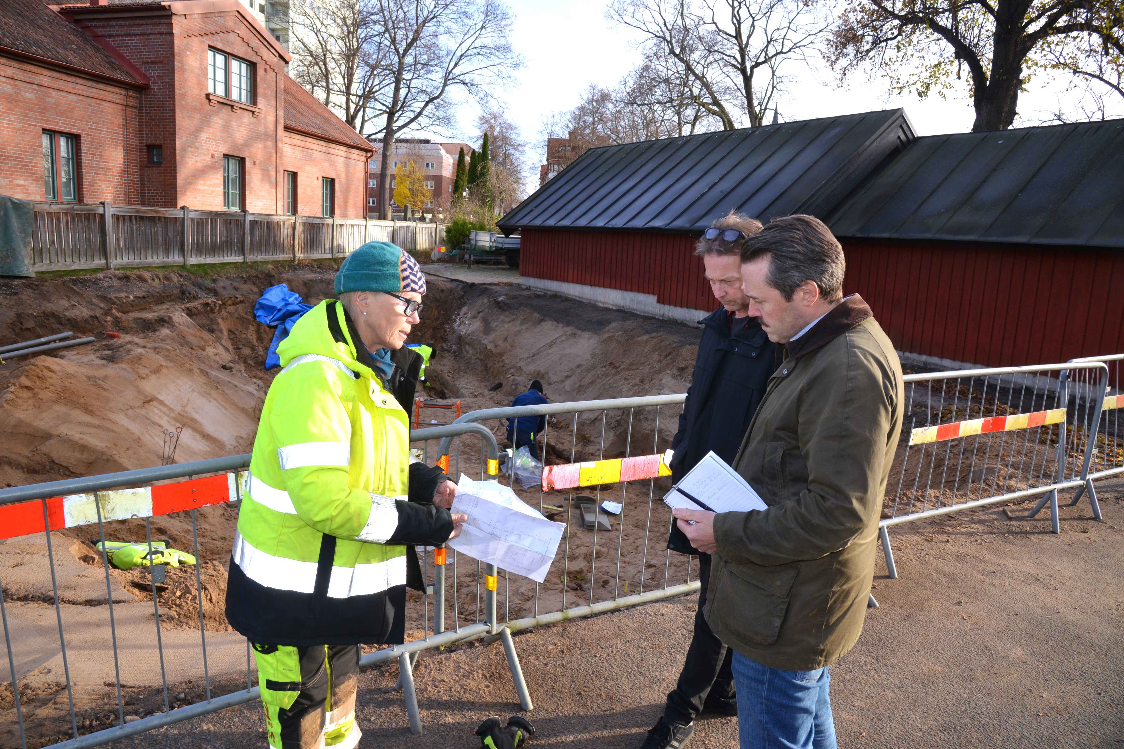 Tre personer står framför en stor grop