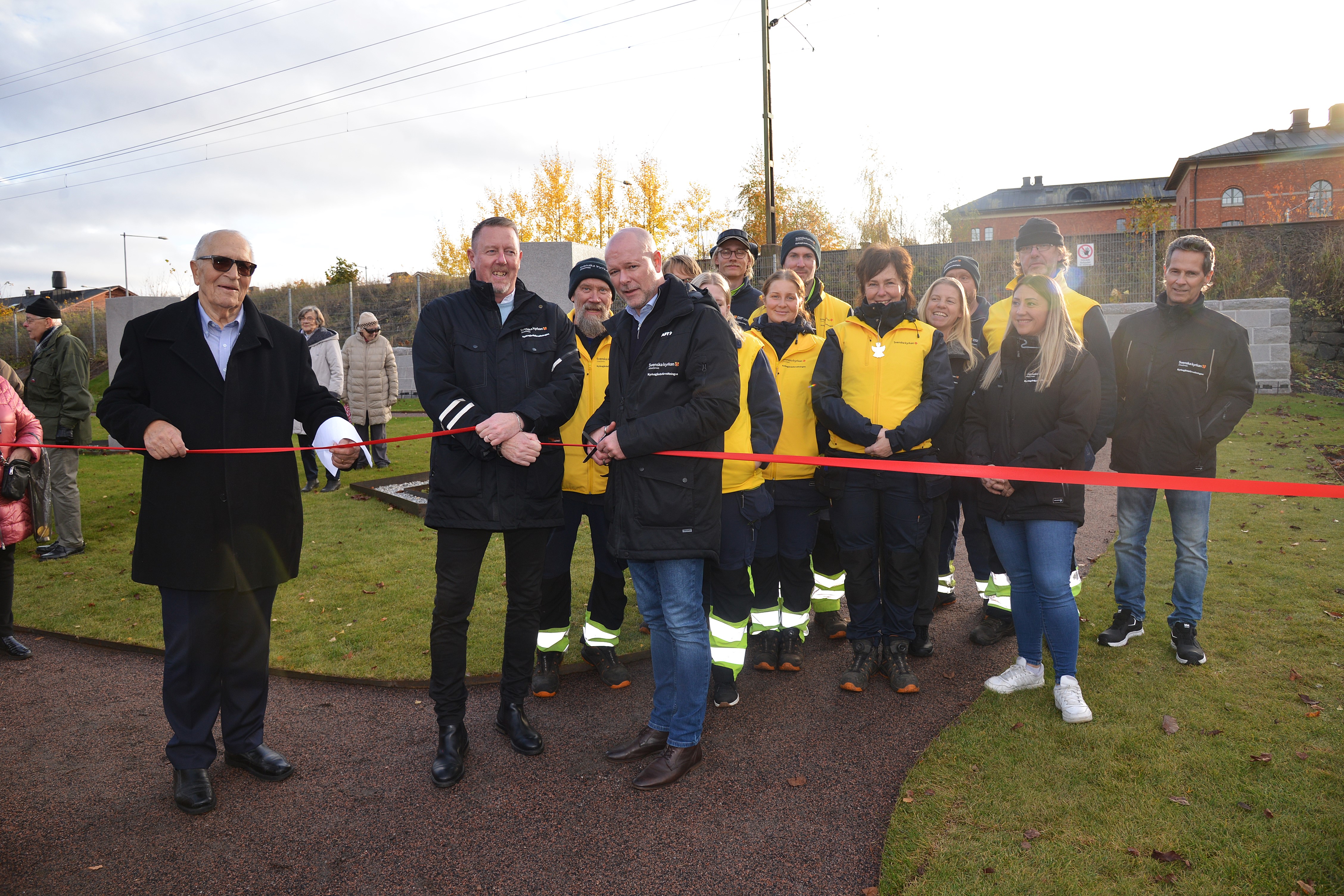 En grupp människor står på en kyrkogård och klipper ett band