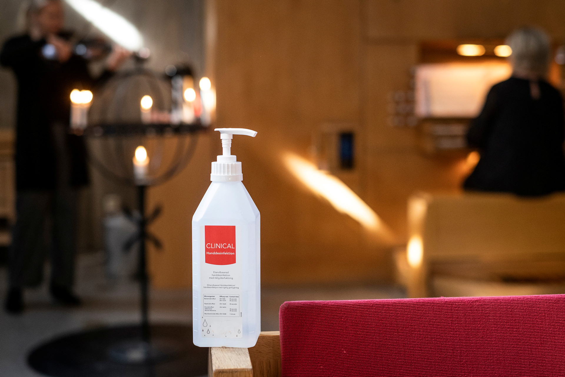 I förgrunden ser du en flaska med handsprit, i bakgrunden  i kyrksalen