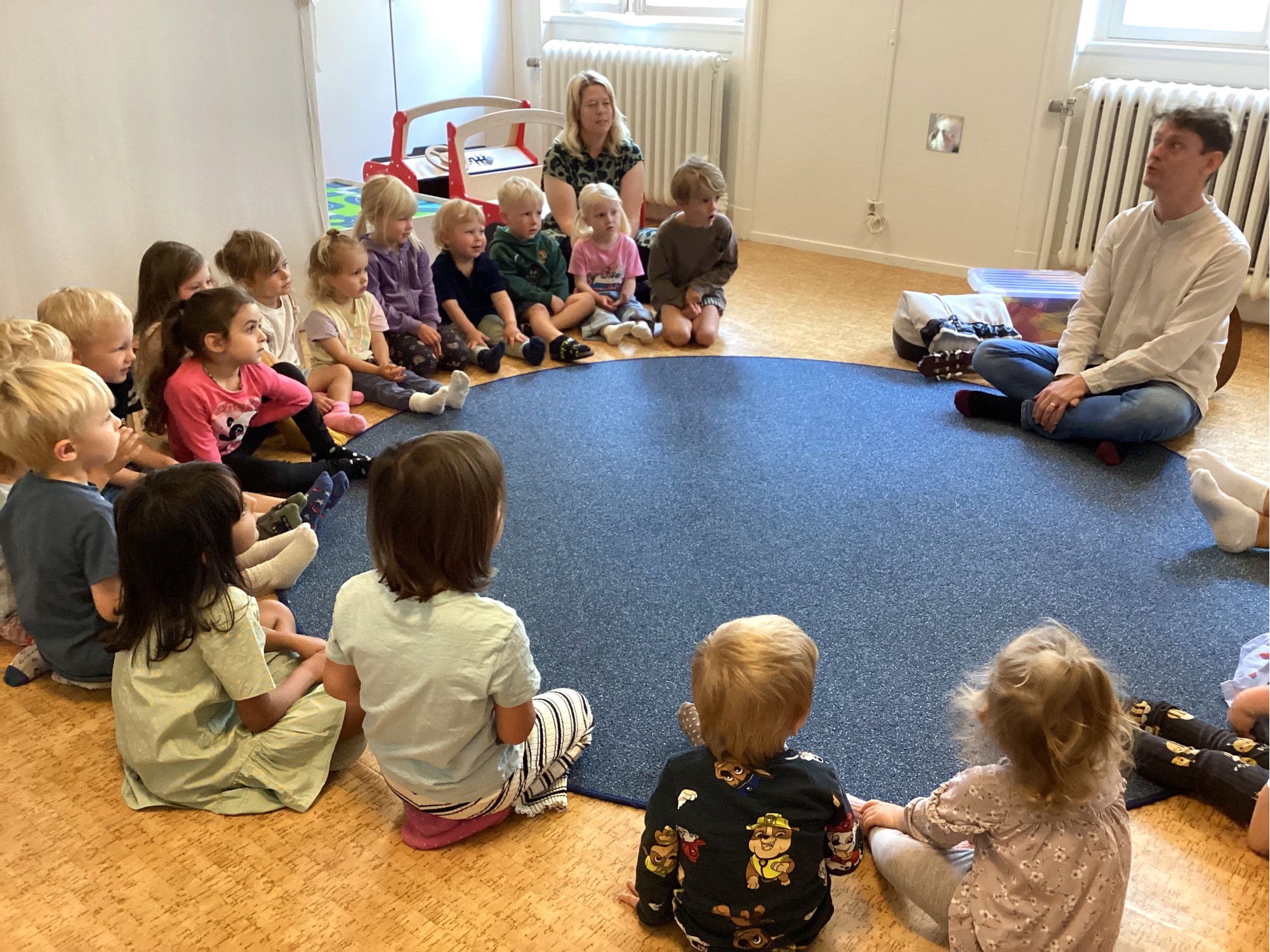 En stor grupp barn sitter i en ring på golvet