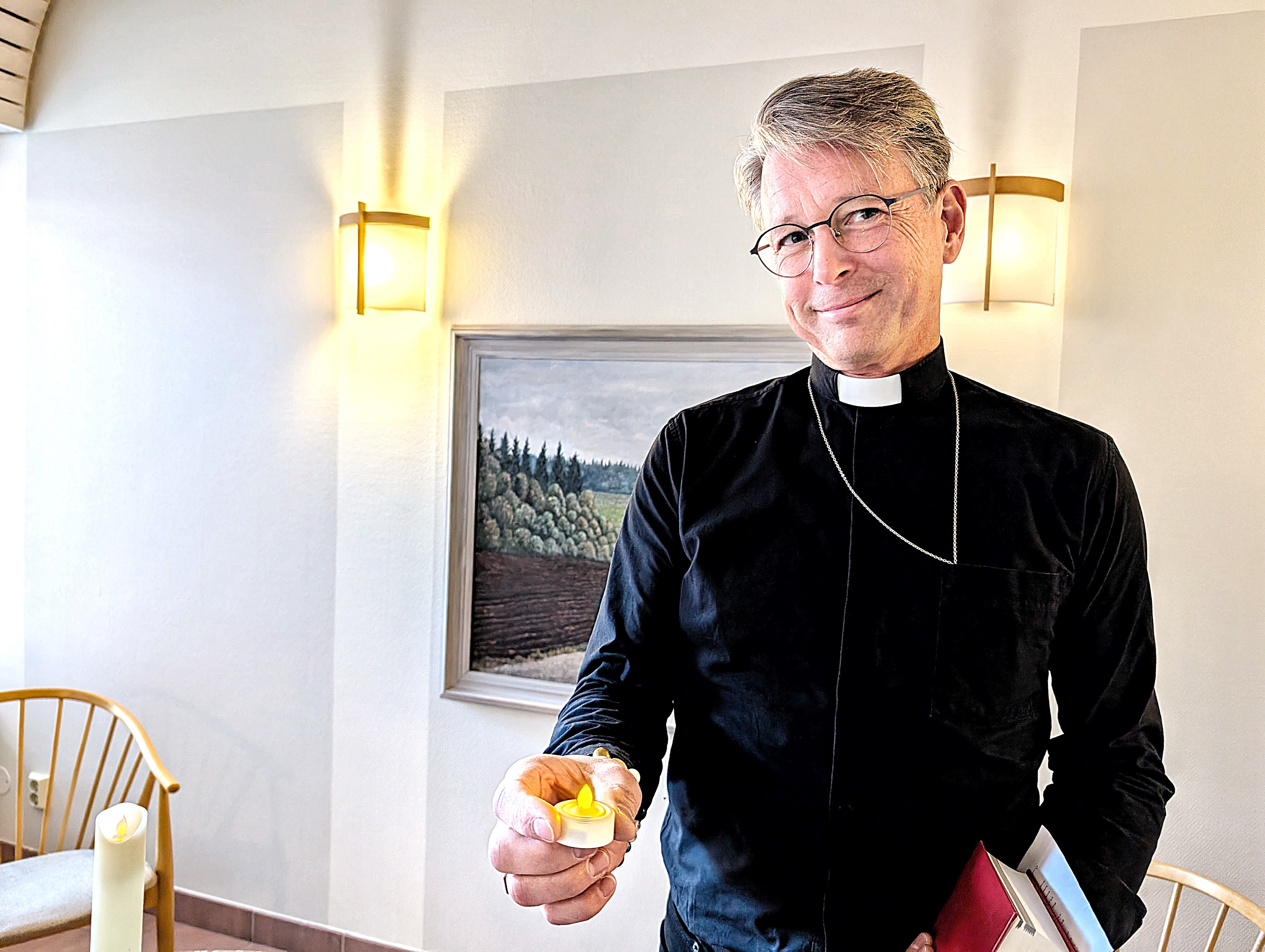 En man i prästkläder står med ett ljus i handen