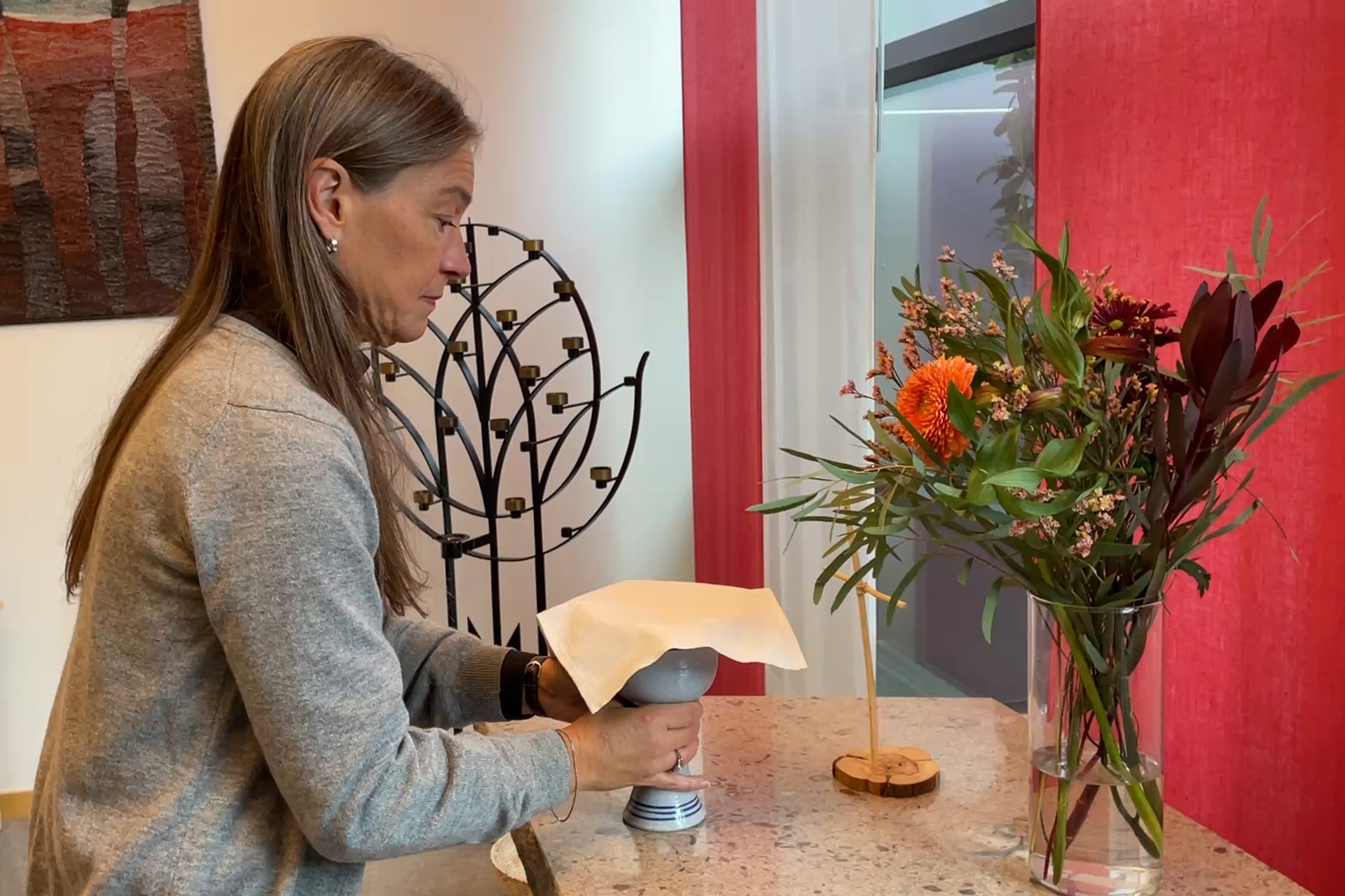 En person ställer fram nattvardskalk och oblat på ett altare med ett kors på.