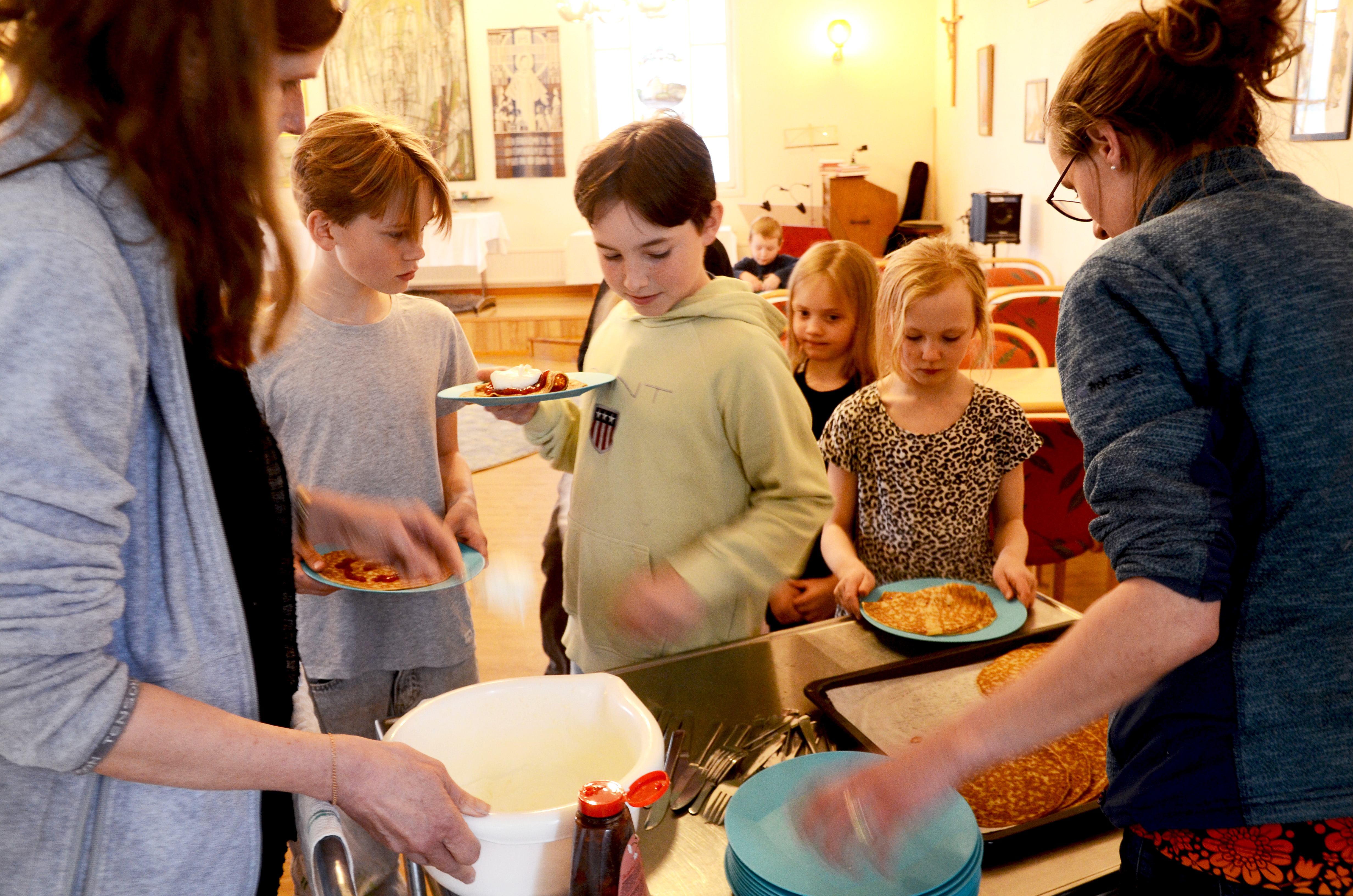 Kyrkoherden och församlingspedagogen serverar pannkakor till några barn.