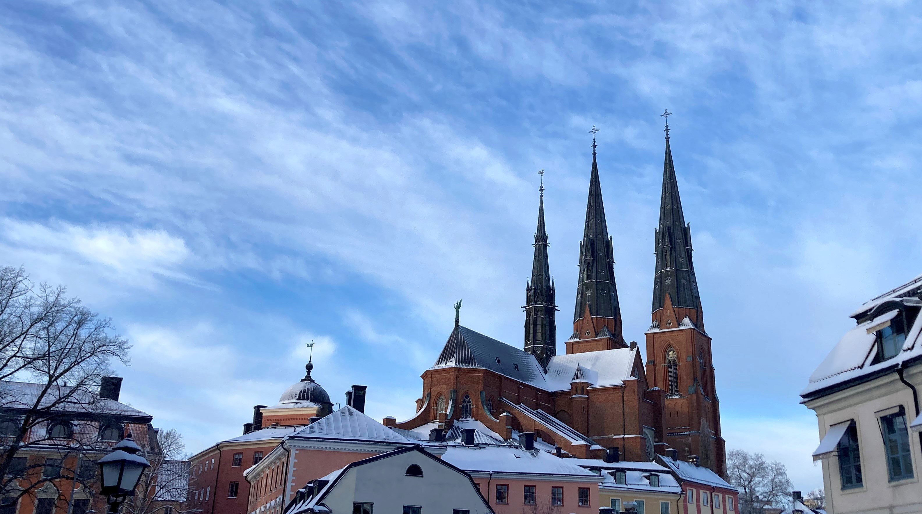 Uppsala domkyrka sedd från Gamla torget i nordost, med ett lätt snötäcke på taket och tornen som avtecknar sig mot en blå himmel med fjäderlätta moln.