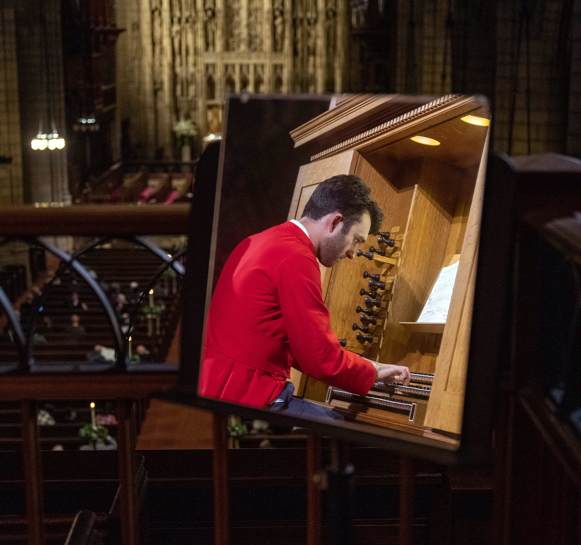 Nicolas Haigh i röd käpa spelar orgel i en varmt dunkel kyrkomiljö.