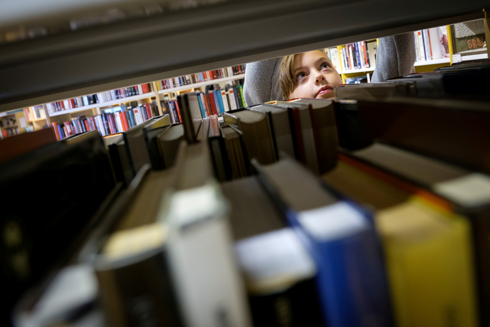 ett barn tittar upp över böcker i en bokhylla