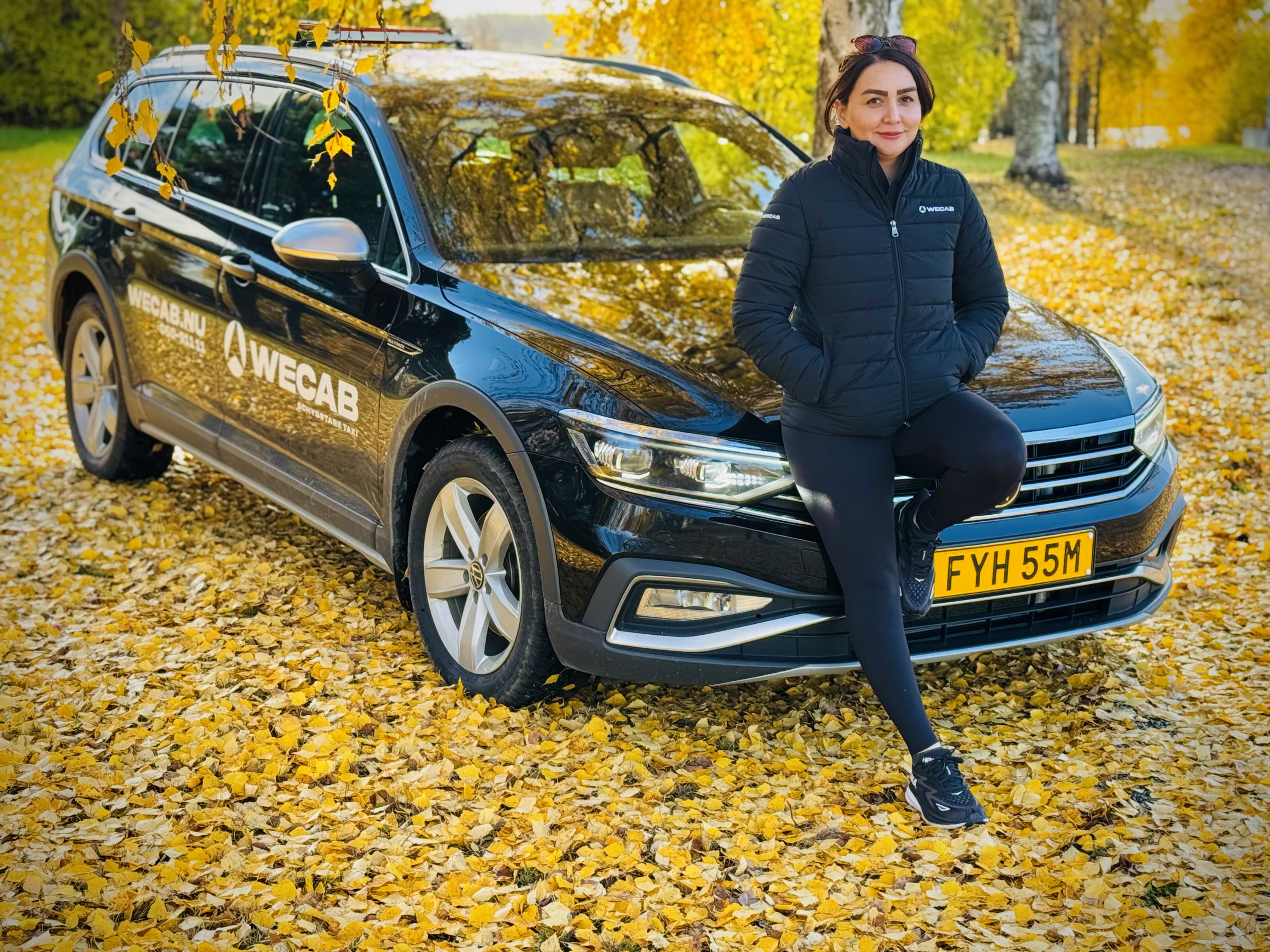 En mörktaxibil och en chaufför som står lutad mot huven.