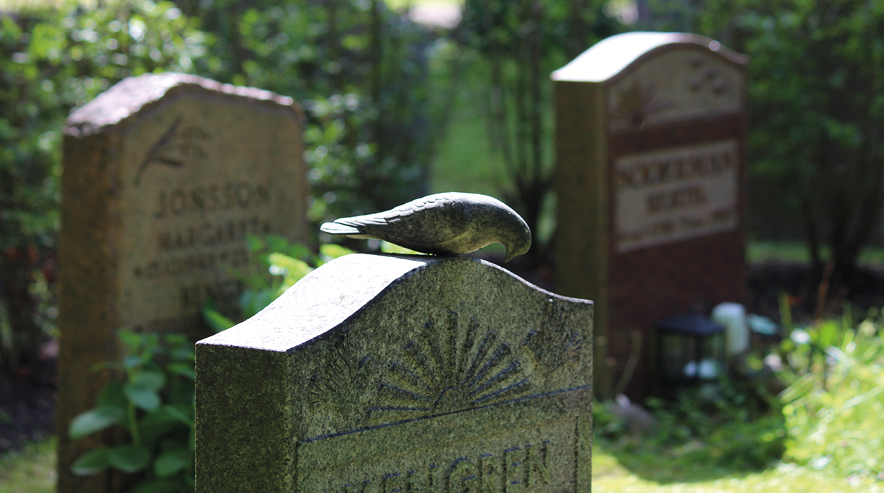 Närbild på en gravsten med en fågelskulptur i sten på. 