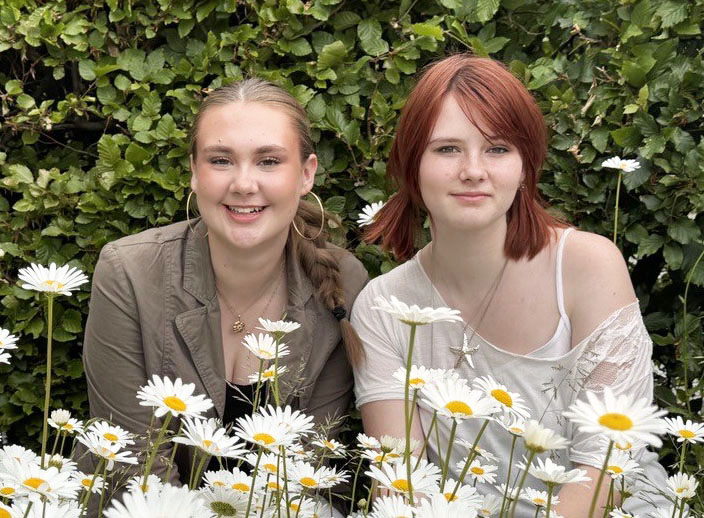 Amanda och Li vid prästkragar och grön buske i bakgrunden
