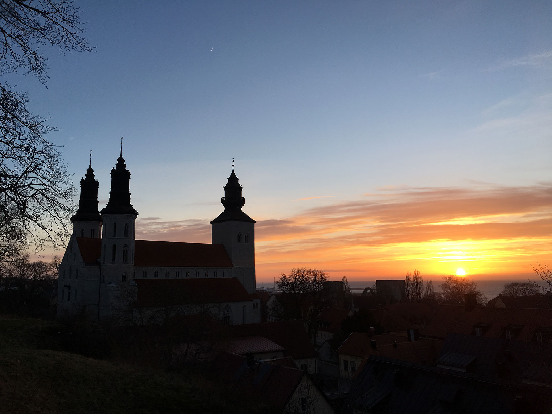 Visby domkyrka i motljus på kvällen. Solen går ner till höger, domkyrkan som siluett till vänster.  