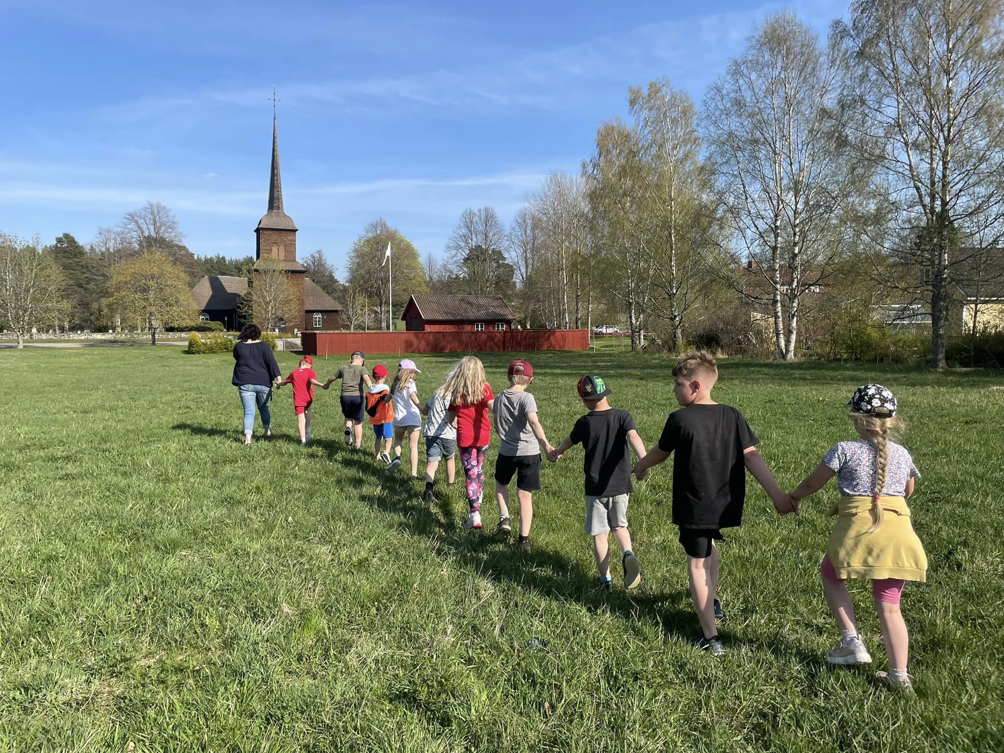 En grupp med barn som går i led och håller hand på en sommaräng