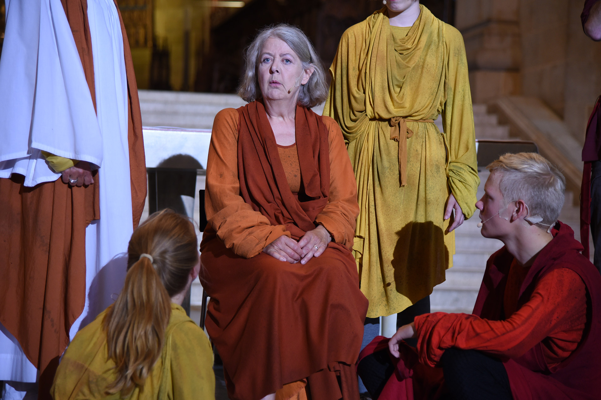 En äldre kvinna sitter och runt henne är flera yngre samlade.