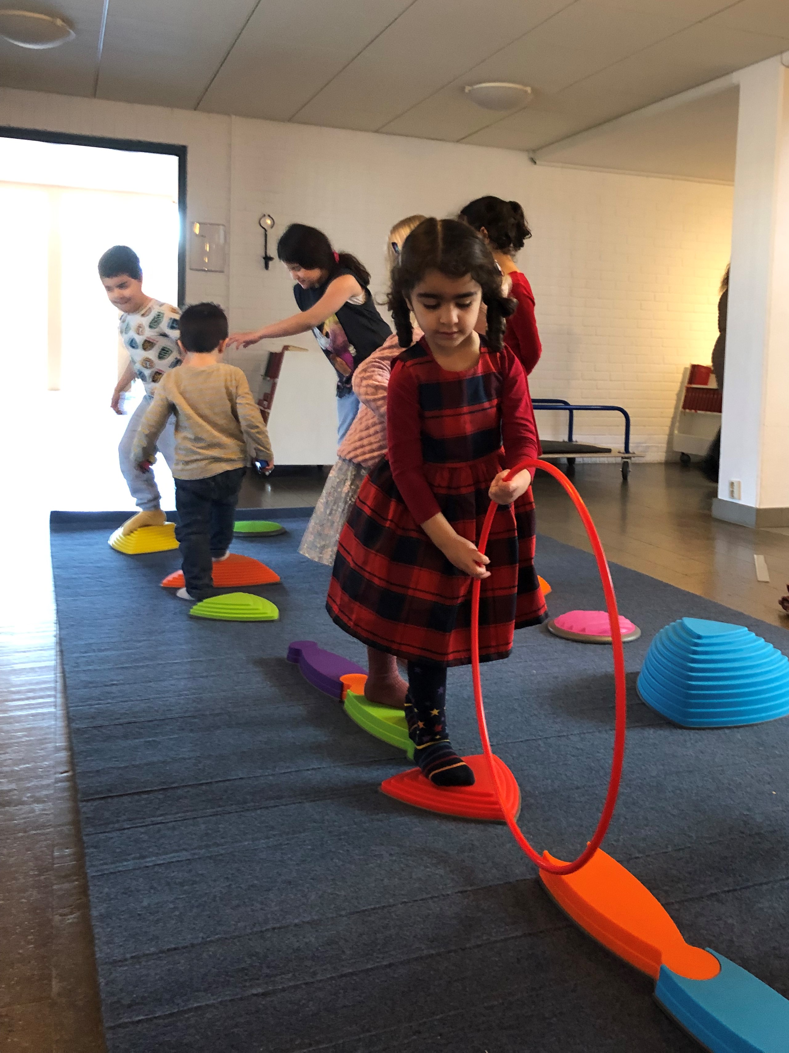 Barn leker på en gymnastikmatta. De balanserar på olika saker och ett barn håller i en rockring.
