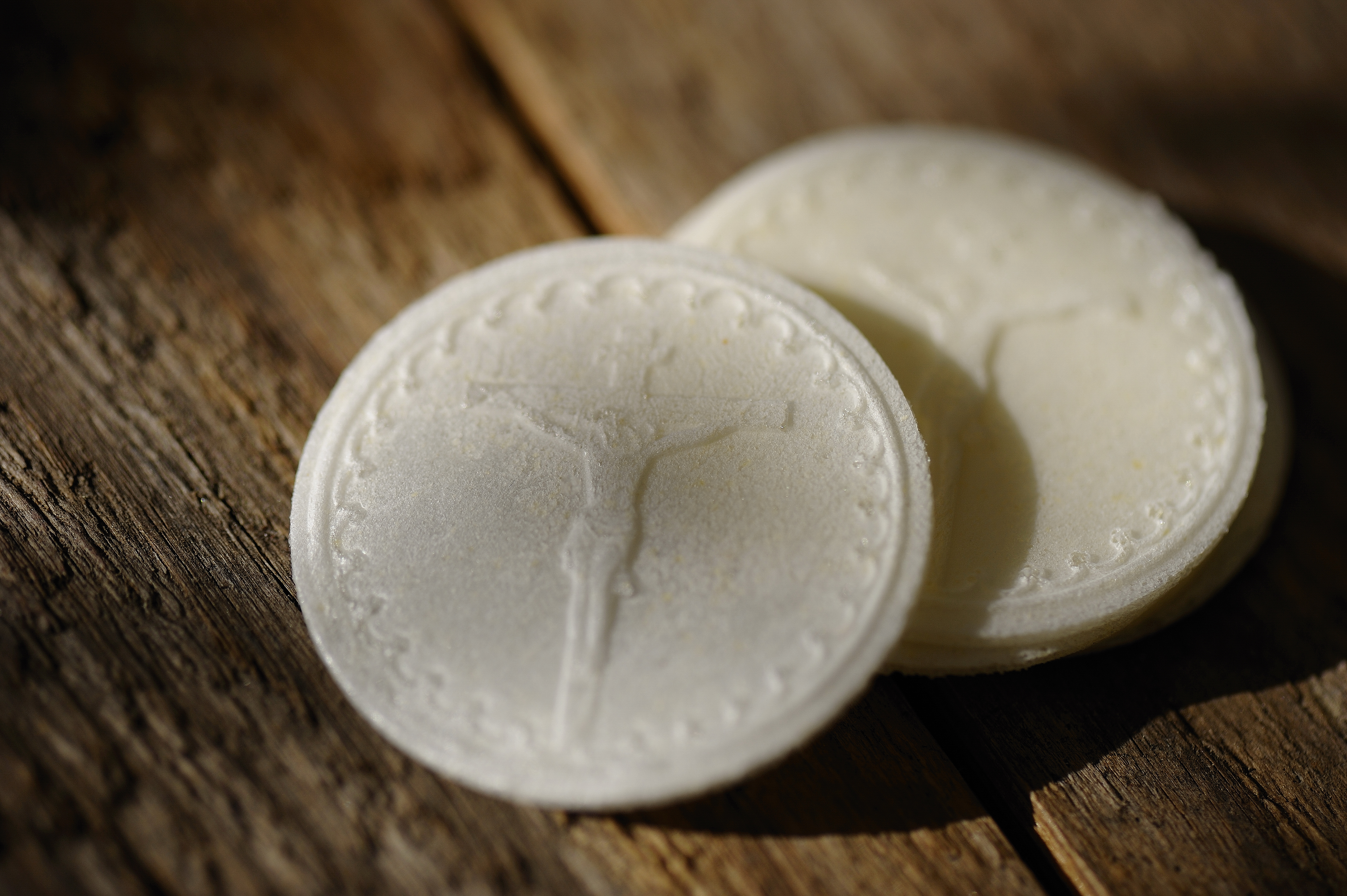 Två oblater ligger på ett bord. På det övre oblatet ser man Kristus på korset.