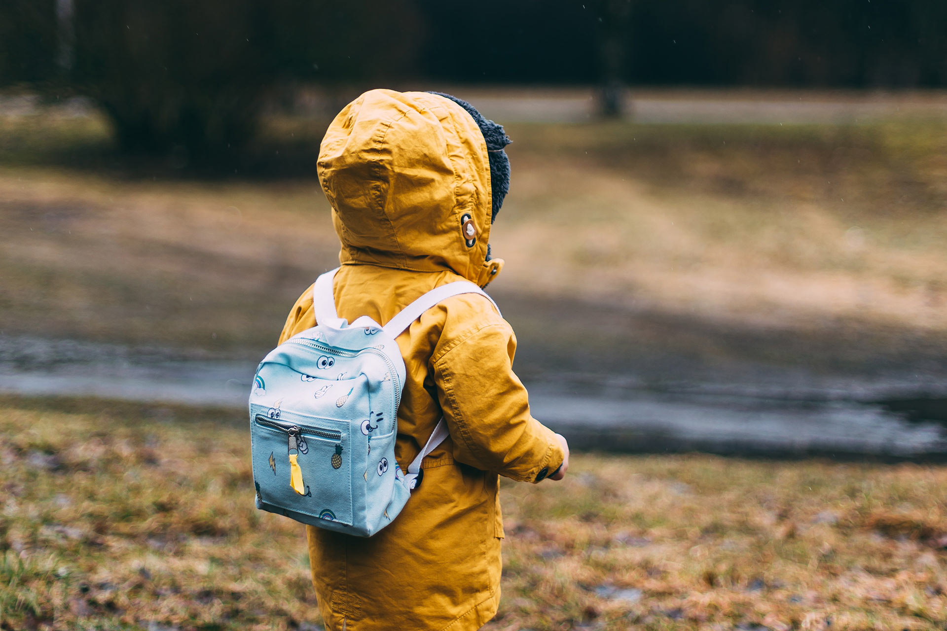 Barn i gul vinterjacka och ryggsäck går från kameran.