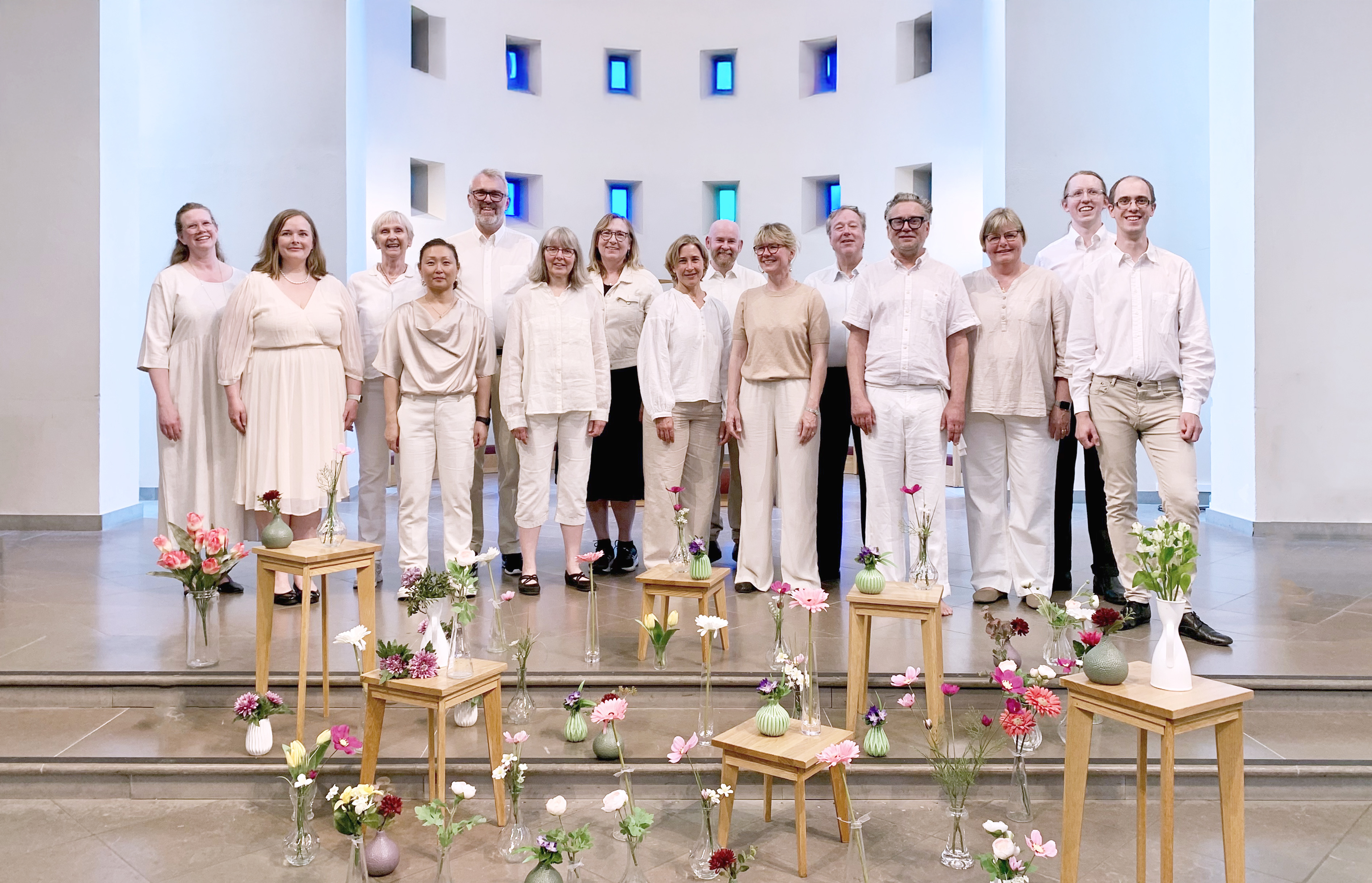 En blandad kör, i huvudsak klädd i vitt, står längst fram i Lundby nya kyrka. På golvet framför dem står snittblommor i vaser.