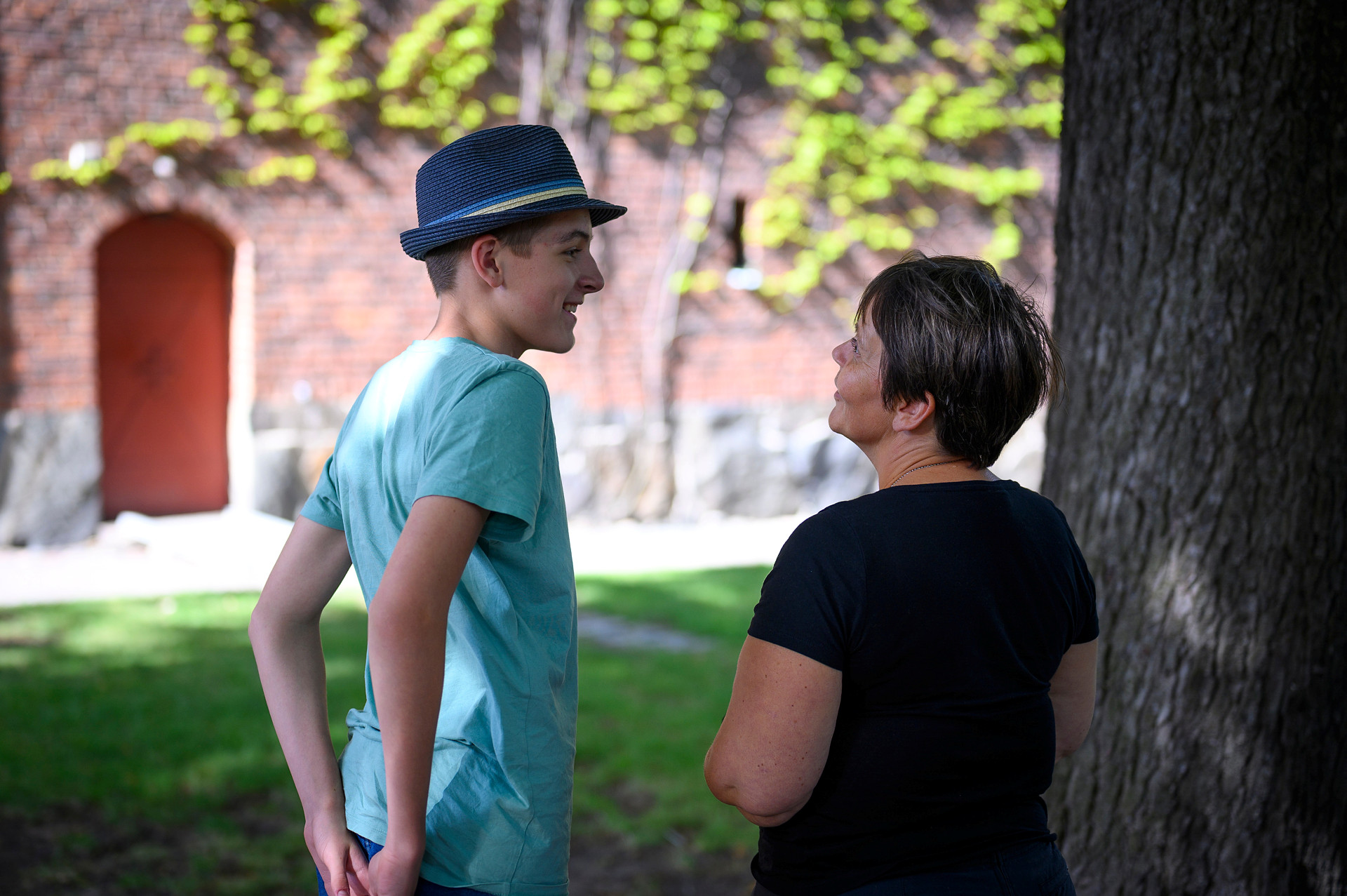 En yngre man och en äldre kvinna samtalar under ett träd. 