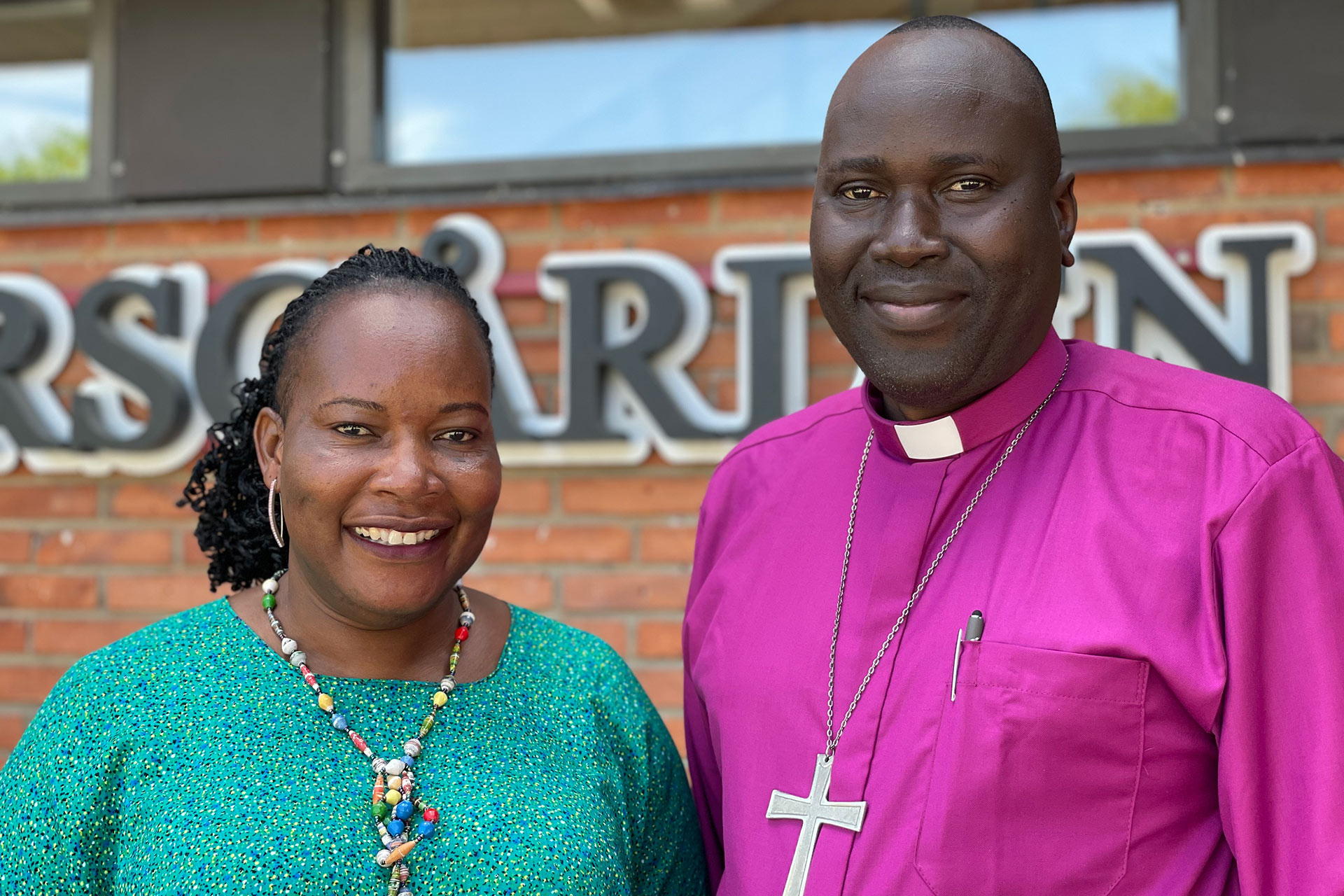 En färgad man i rosa skjorta och stort kors och en färgad kvinna i grön topp.