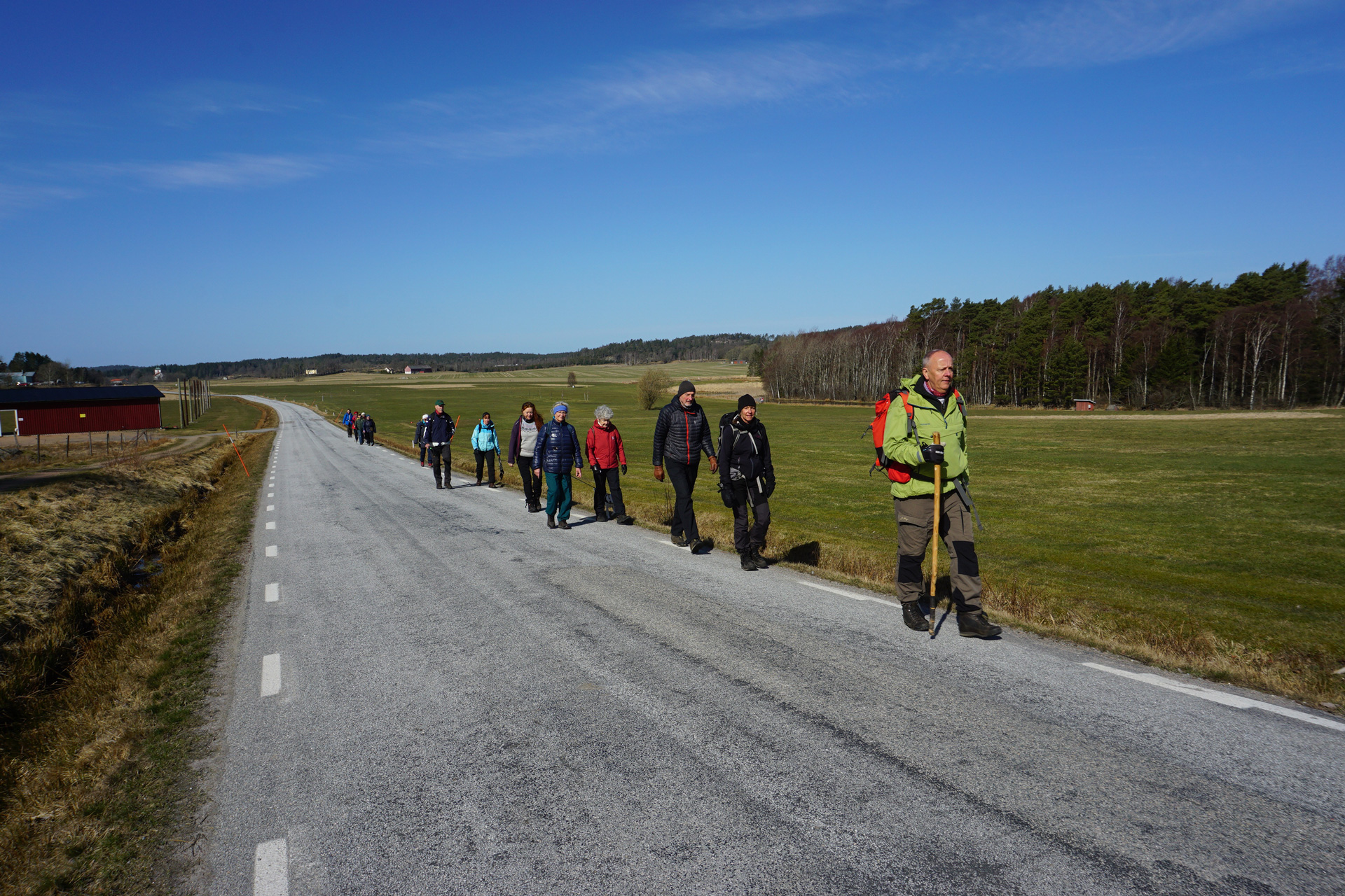 Pilgrimmer på vandring längs en landsväg. Soligt väder och blå himmel. 