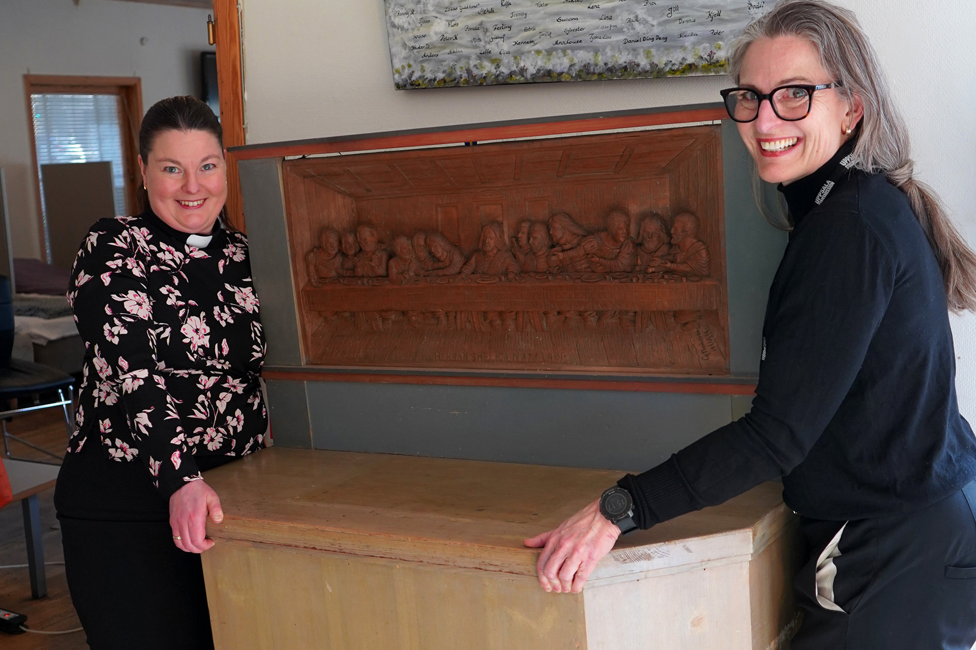 Matilda Helg i blommig skjorta och prästkrage och Agneta Nilsson i svarta kläder och glasögon hjälps åt att lyfta ett altarbord i trä.
