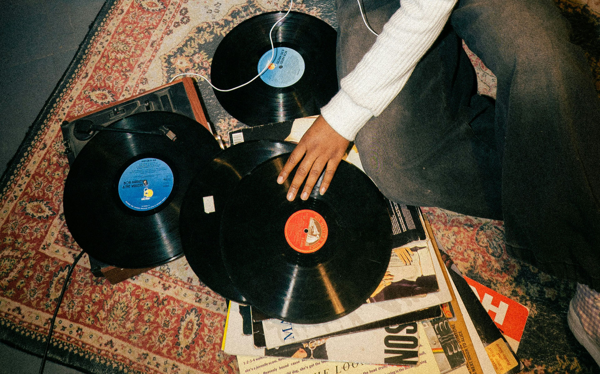 Vinylskivor ligger utspridda på en matta. En hand  är på väg att plocka upp en av skivorna.
