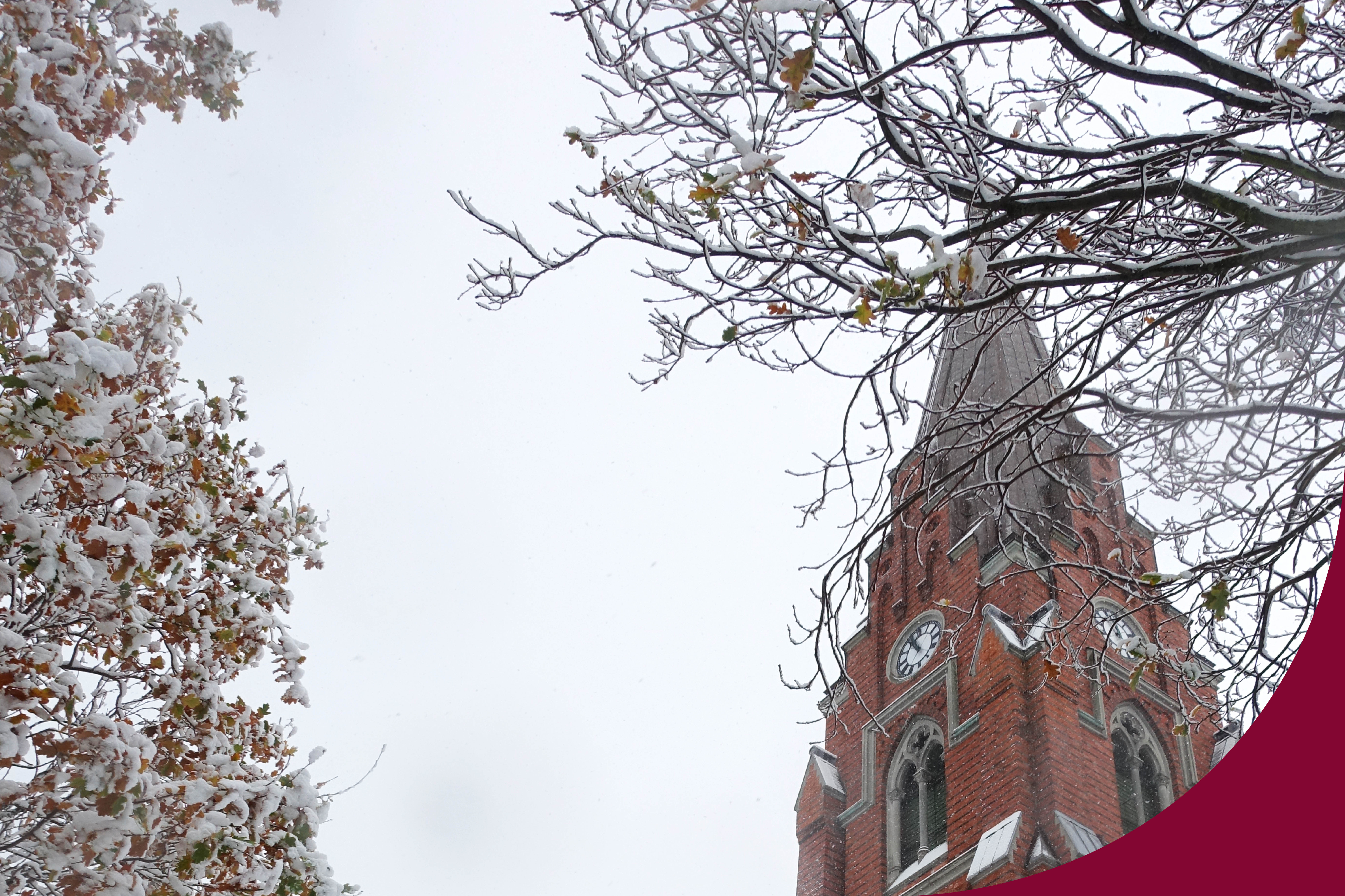 Tornet på Allhelgonakyrkan täckt med snö. I förgrunden ser man grenar med snö på.