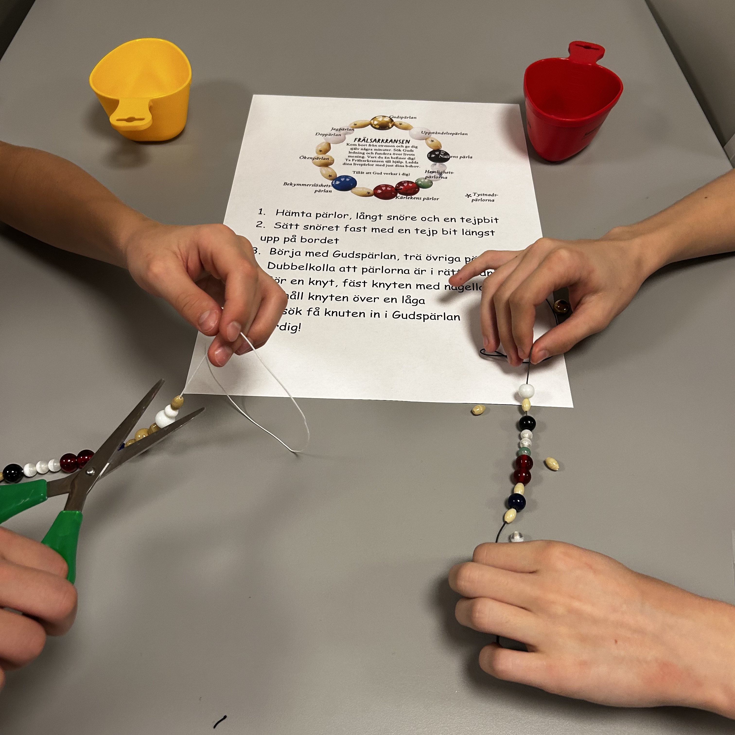 På bilden syns två par händer som håller på att montera ihop armband/frälsarkransar