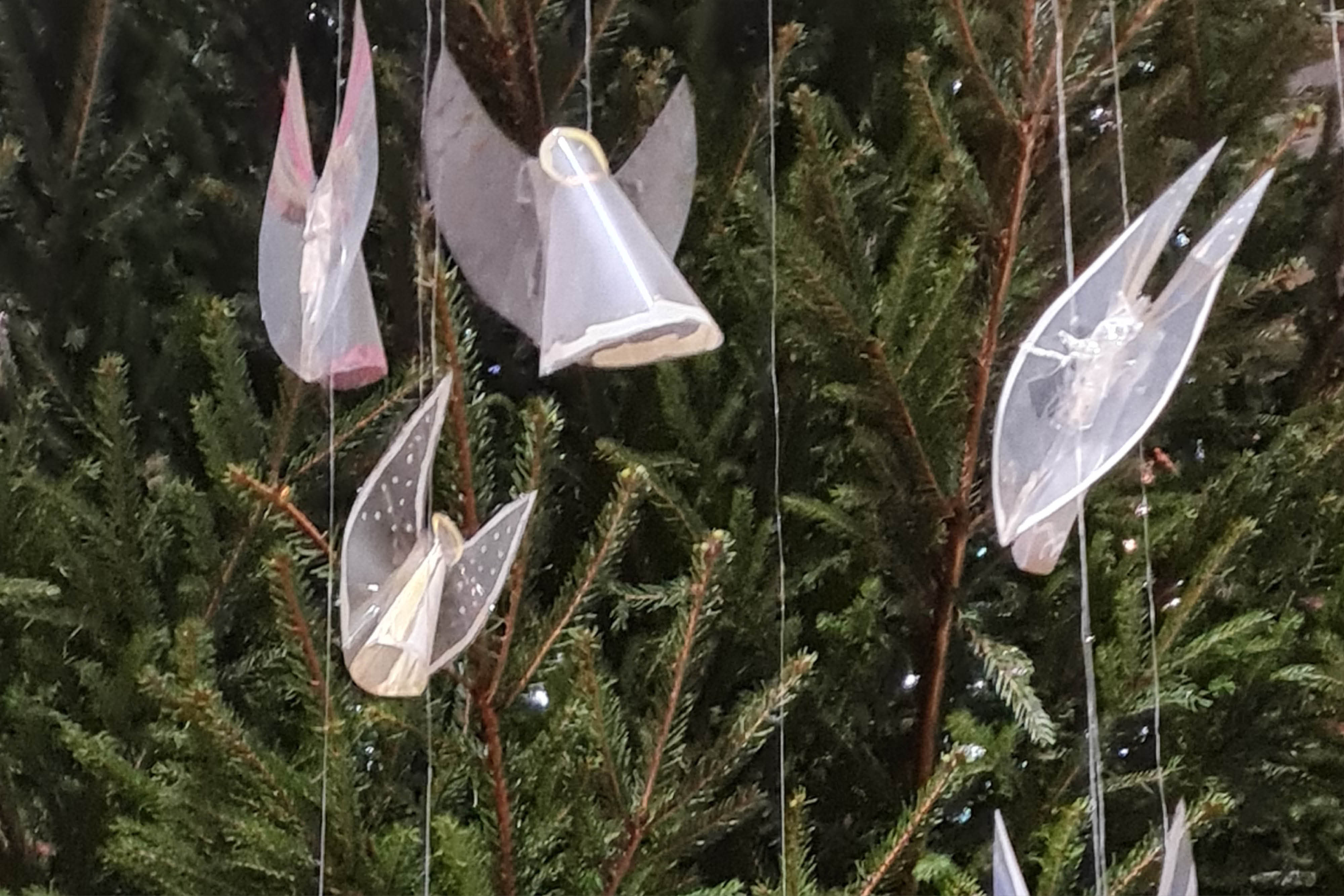 Genomskinliga vita änglar som hänger framför en gran. 