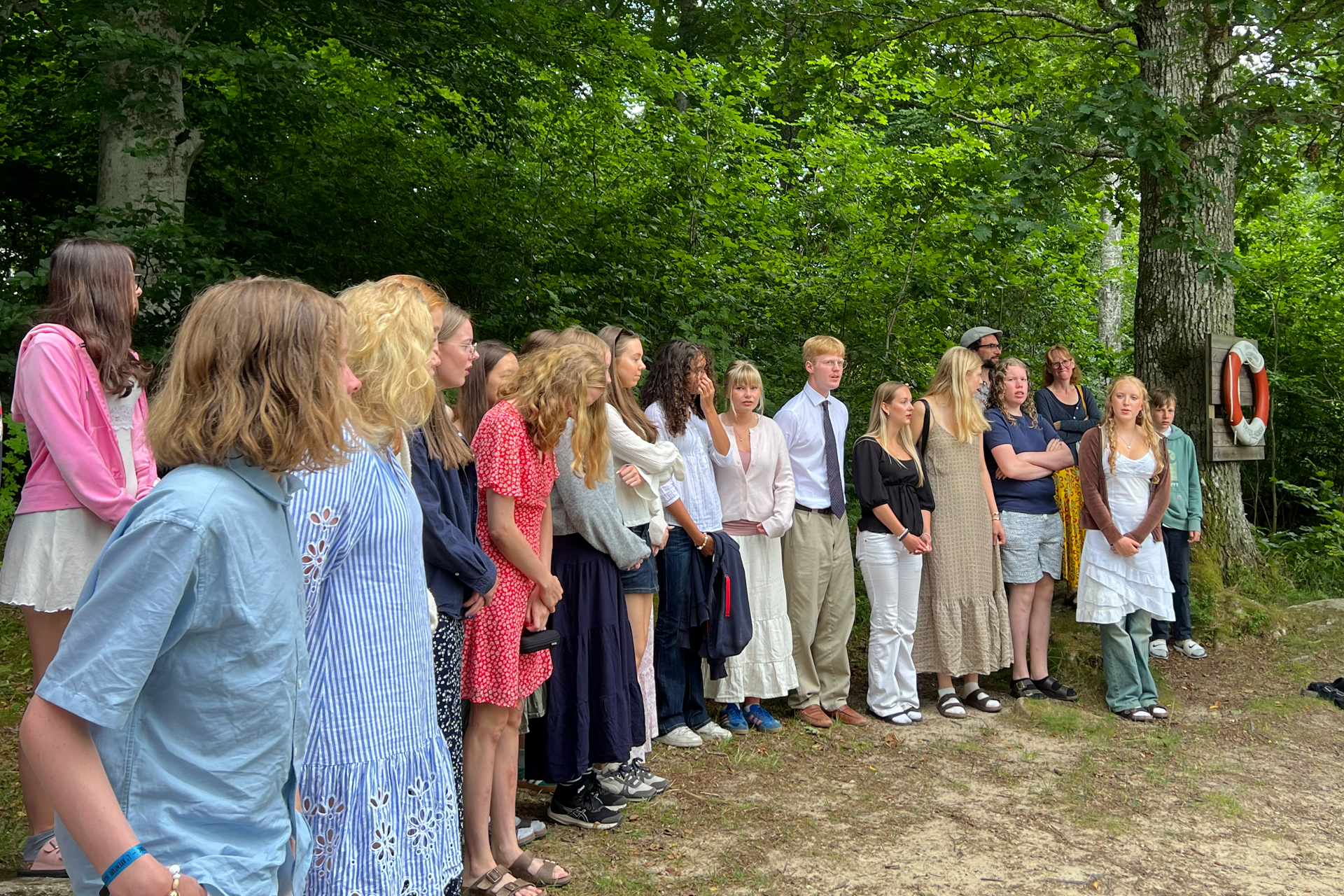 En grupp ungdomar står sommarklädda i en skogsglänta. 