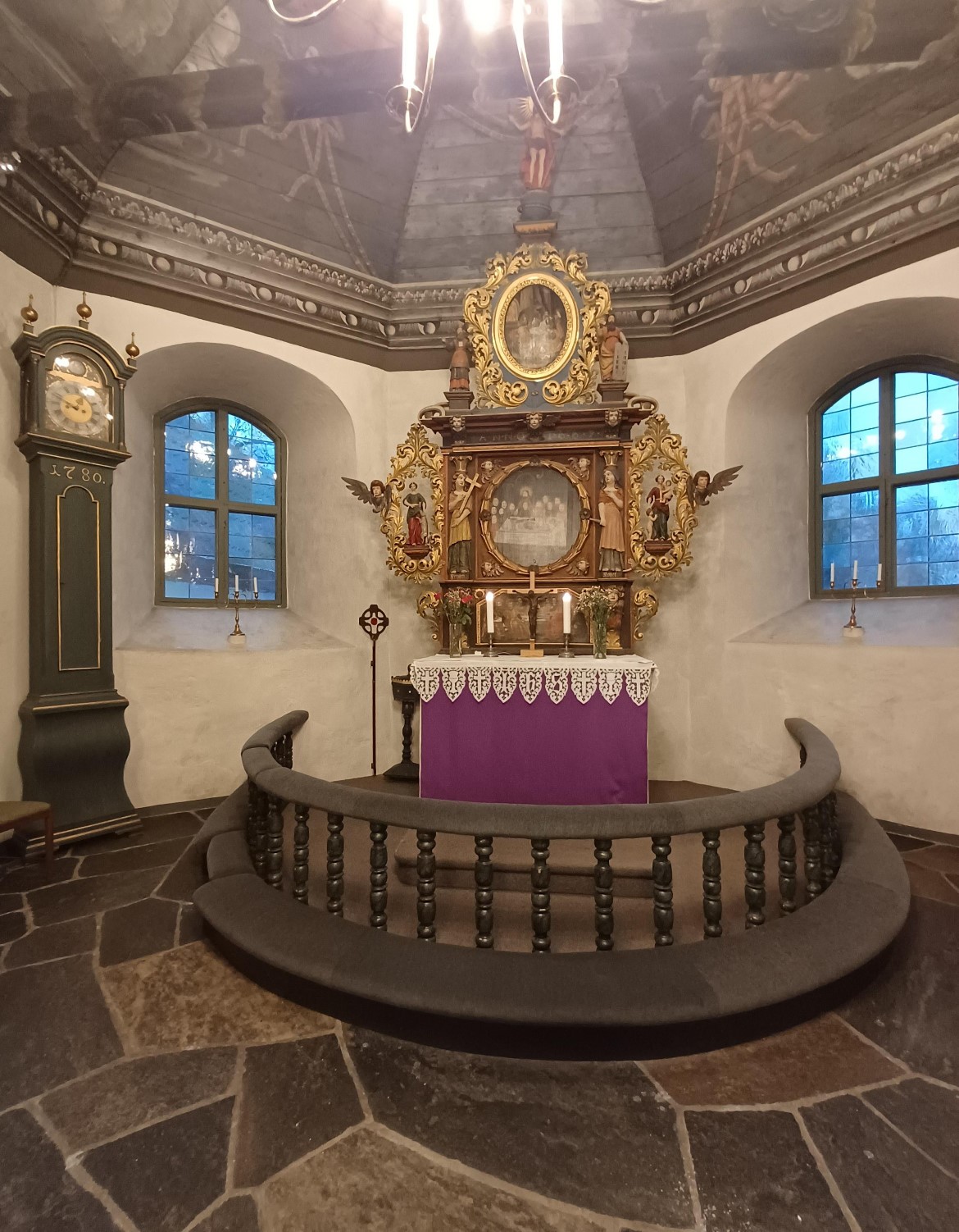 Altaret i Kållereds kyrka. Altarringen är nyklädd med brunt tyg. På altaret hänger lila antipendie. Ett väggur står till vänster.