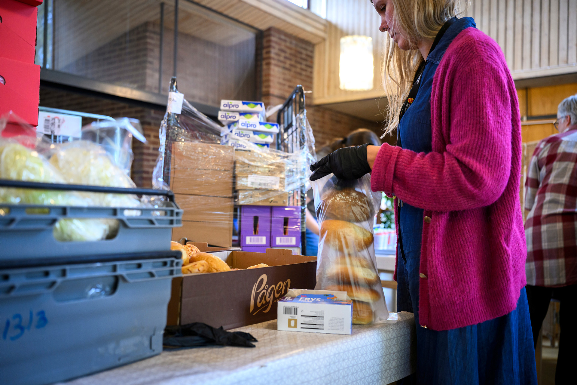 En kvinna står vid en disk med matvaror och lägger bröd i en påse.