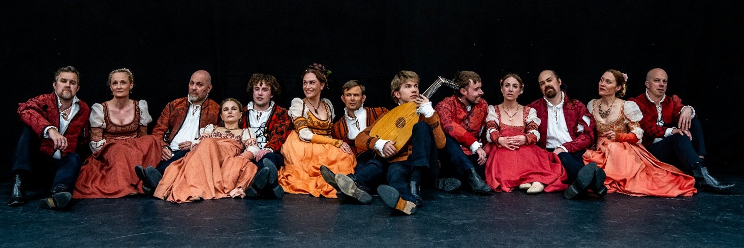 Lång bild på sångare ur Romeo och Juliakören. Svart bakgrund färgglada historiska kläder.