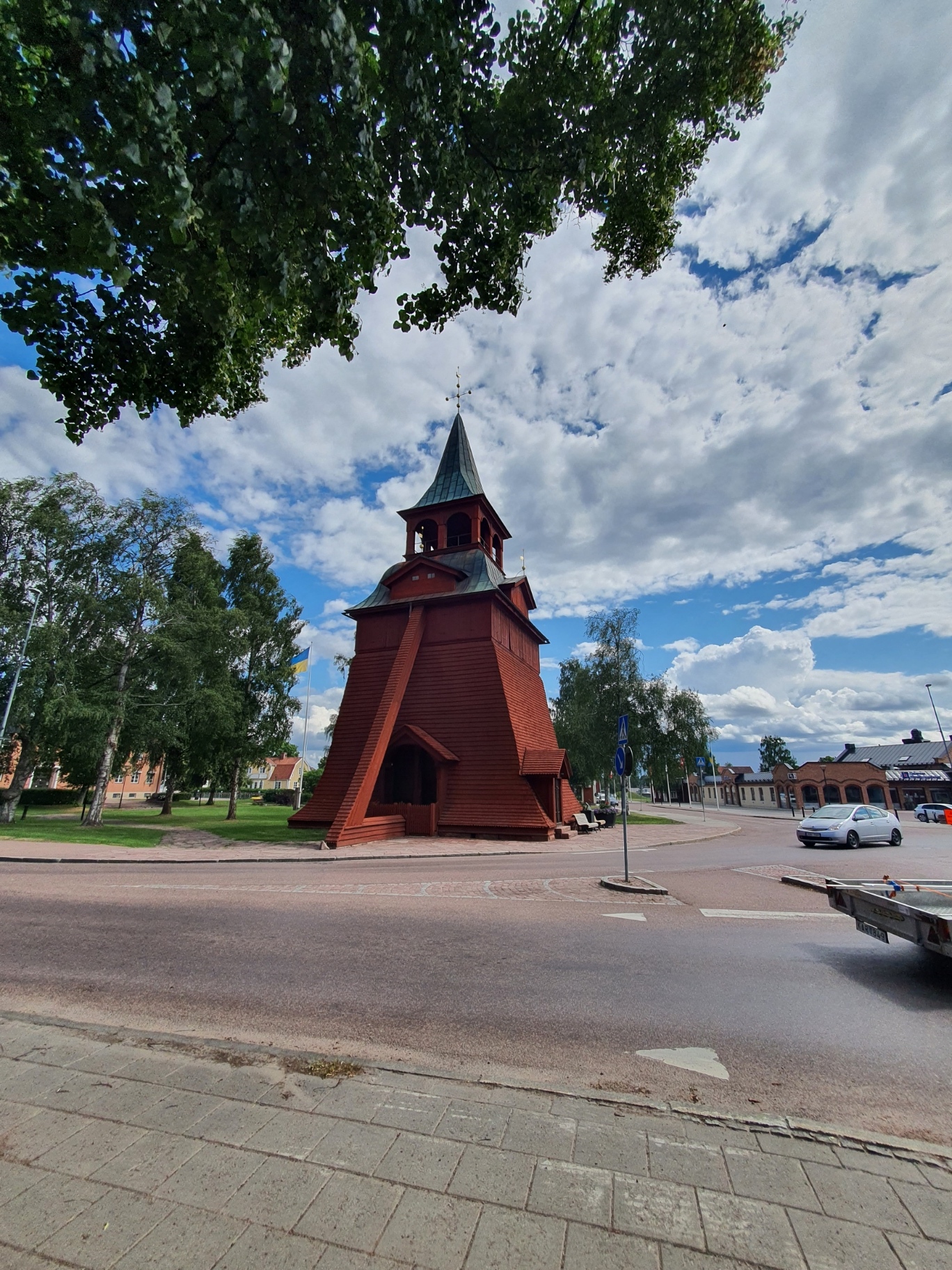 vy över klockstapel rödmålad med grönt koppartak en sommardag
