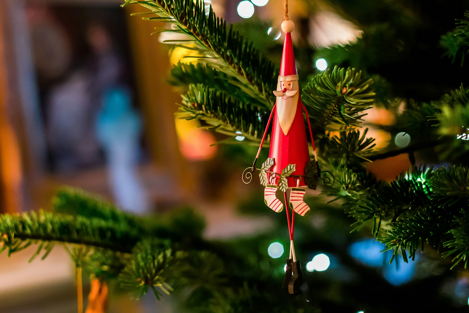 Julgransprydnad i forma av en tomte som hänger i klädd julgran. Julkänsla.