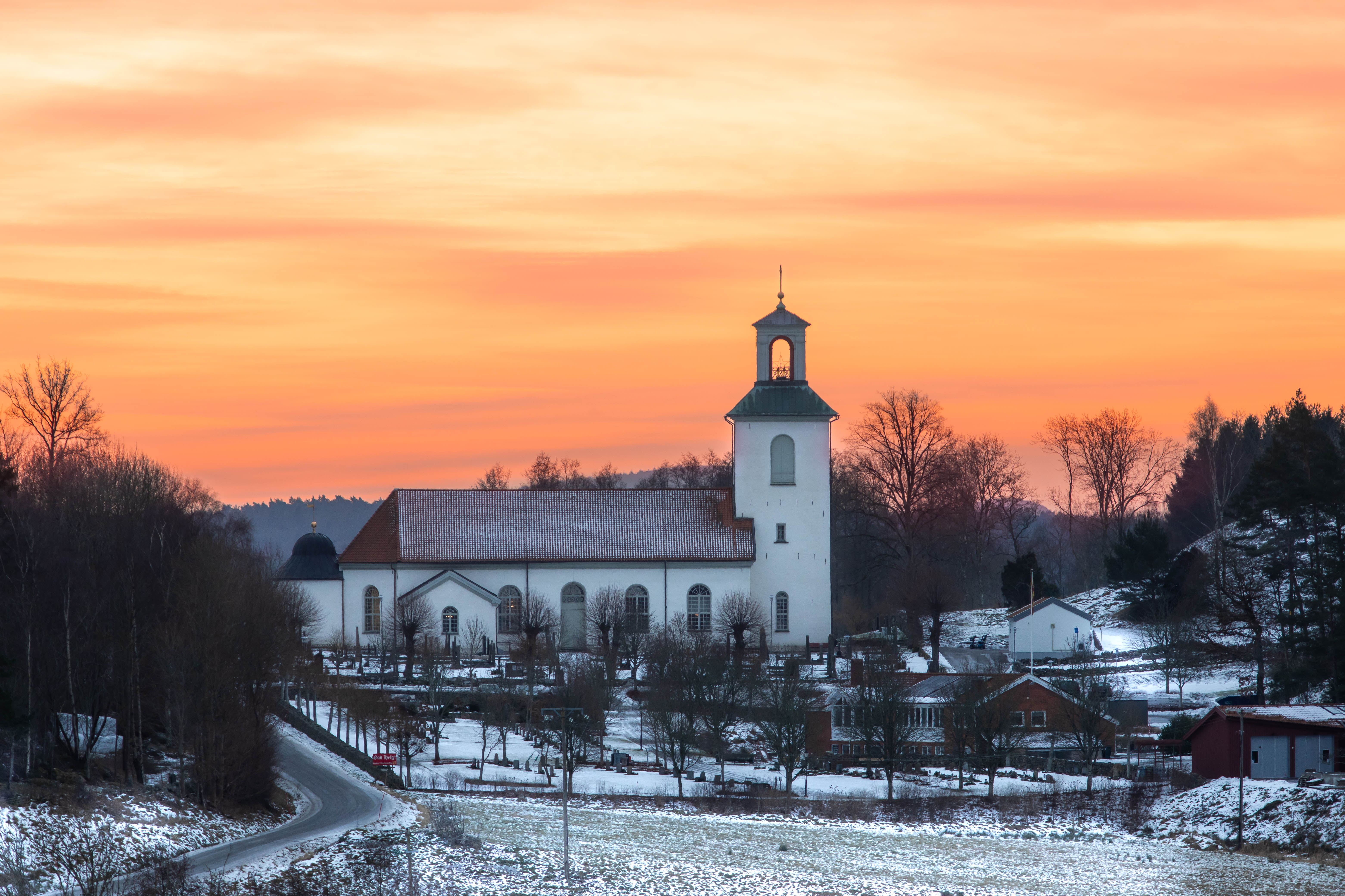 Orange himmel över vit kyrka, snö på marken.