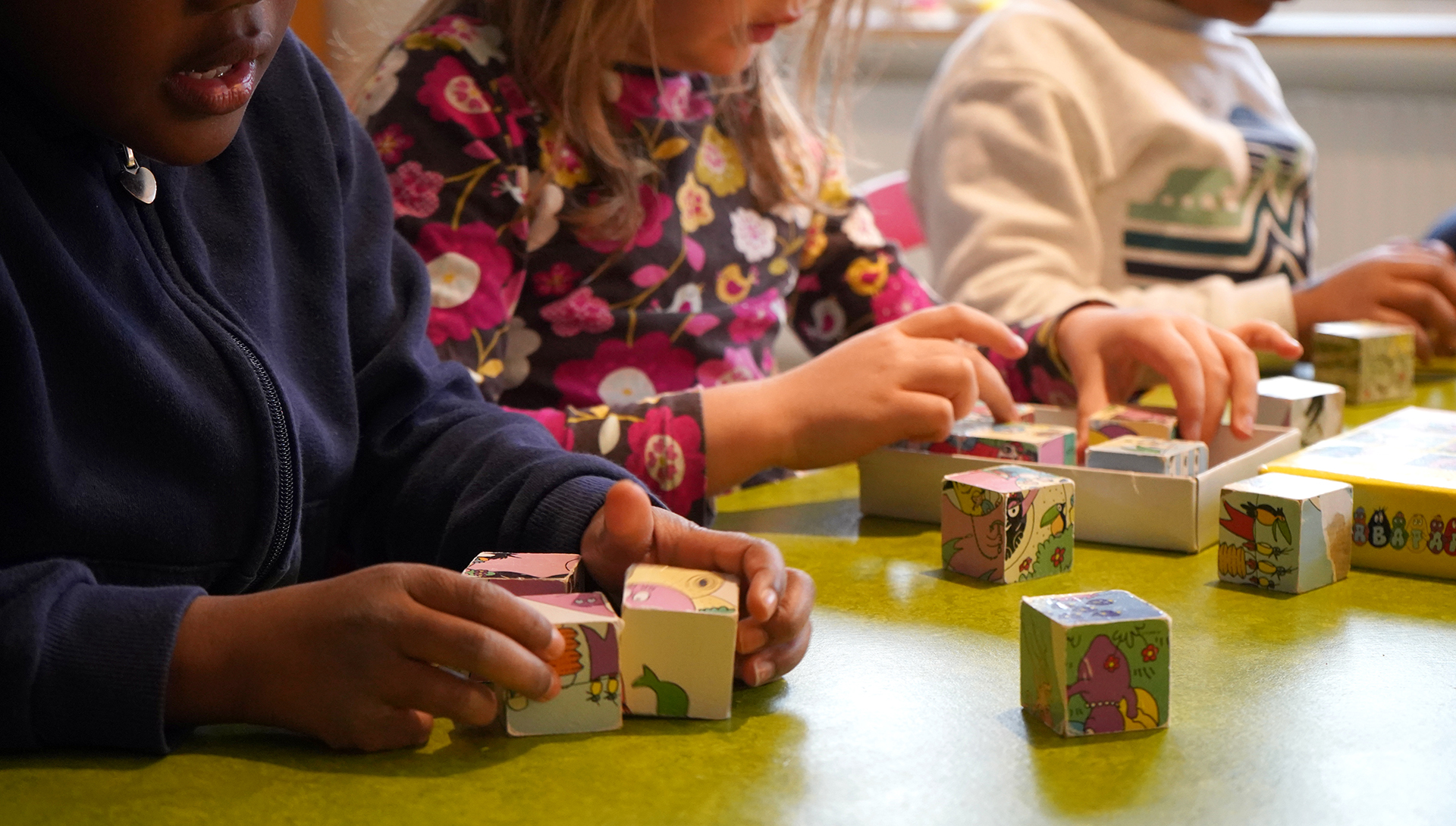 Tre förskolebarn syns vid ett bord där de tillsammans lägger pussel med olika klossar.
