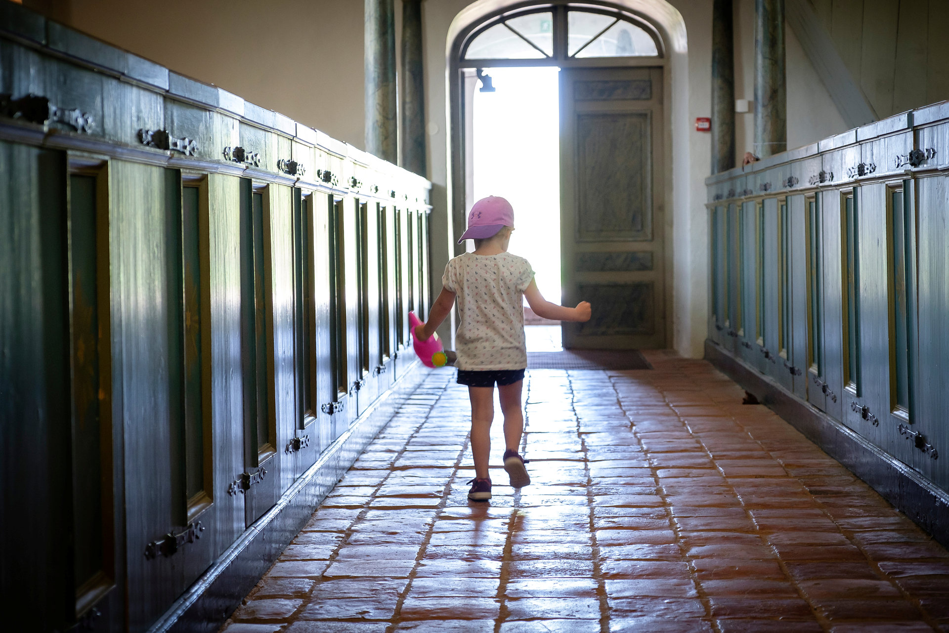 Litet barn i lila keps springer längs altargången i kyrkan mot den öppna kyrkporten.