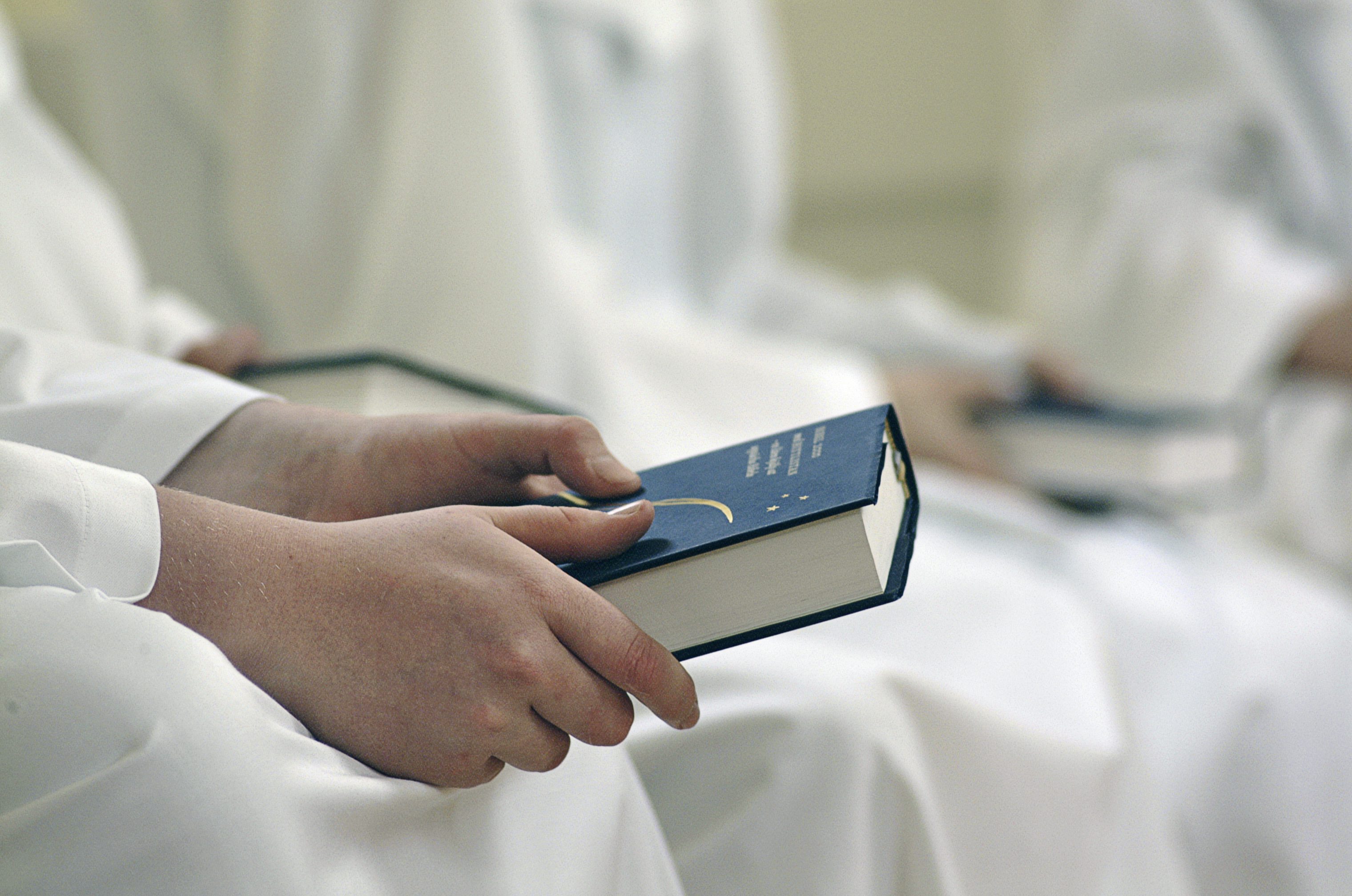 Konfirmander i vita kåpor sitter med varsin psalmbok i handen.