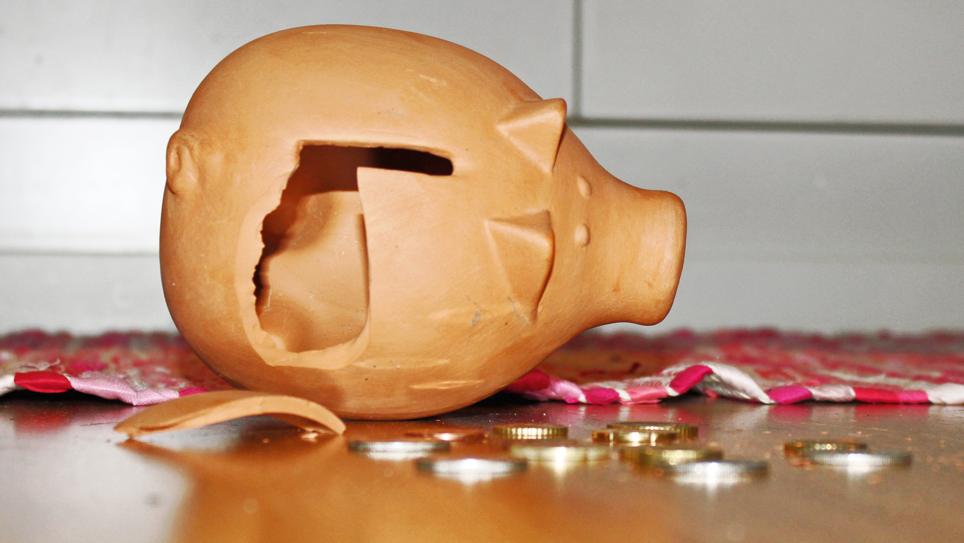 En krossad spargris ligger på golvet, några mynt ligger utspridda bredvid.