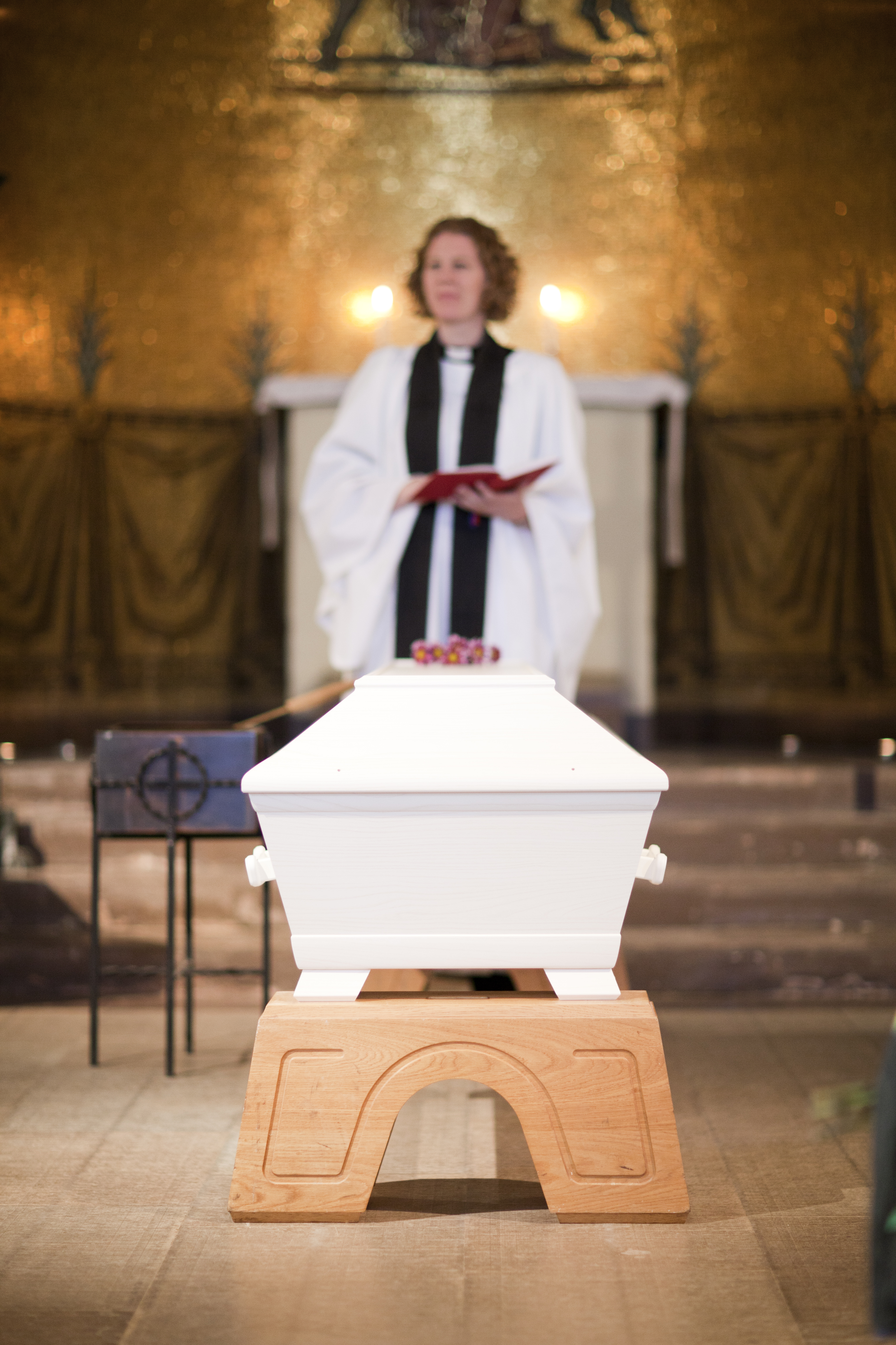En präst står bakom en vit kista inne i en kyrka.