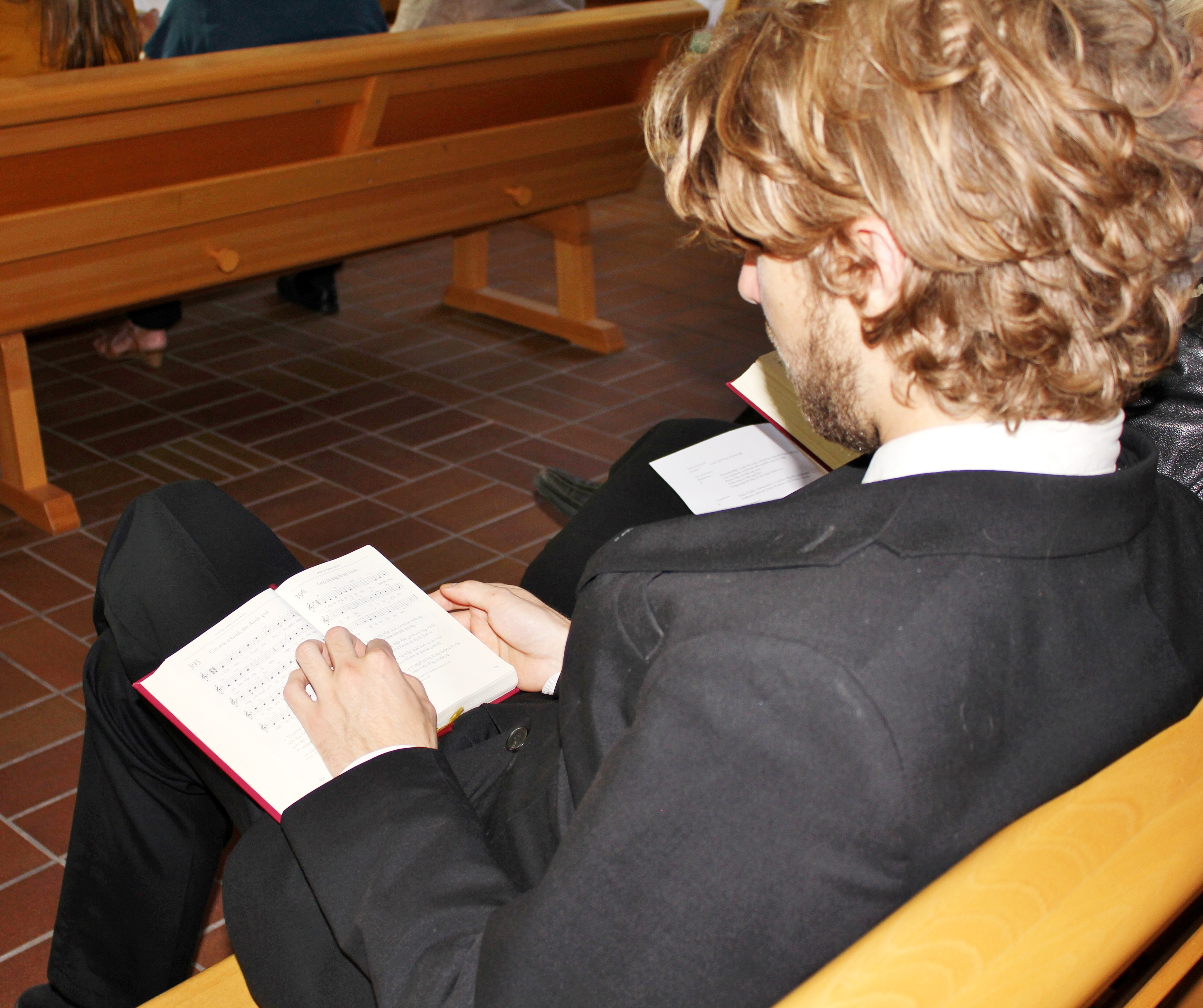 En man i kostym sitter i en kyrkbänk med en psalmbok i knät.