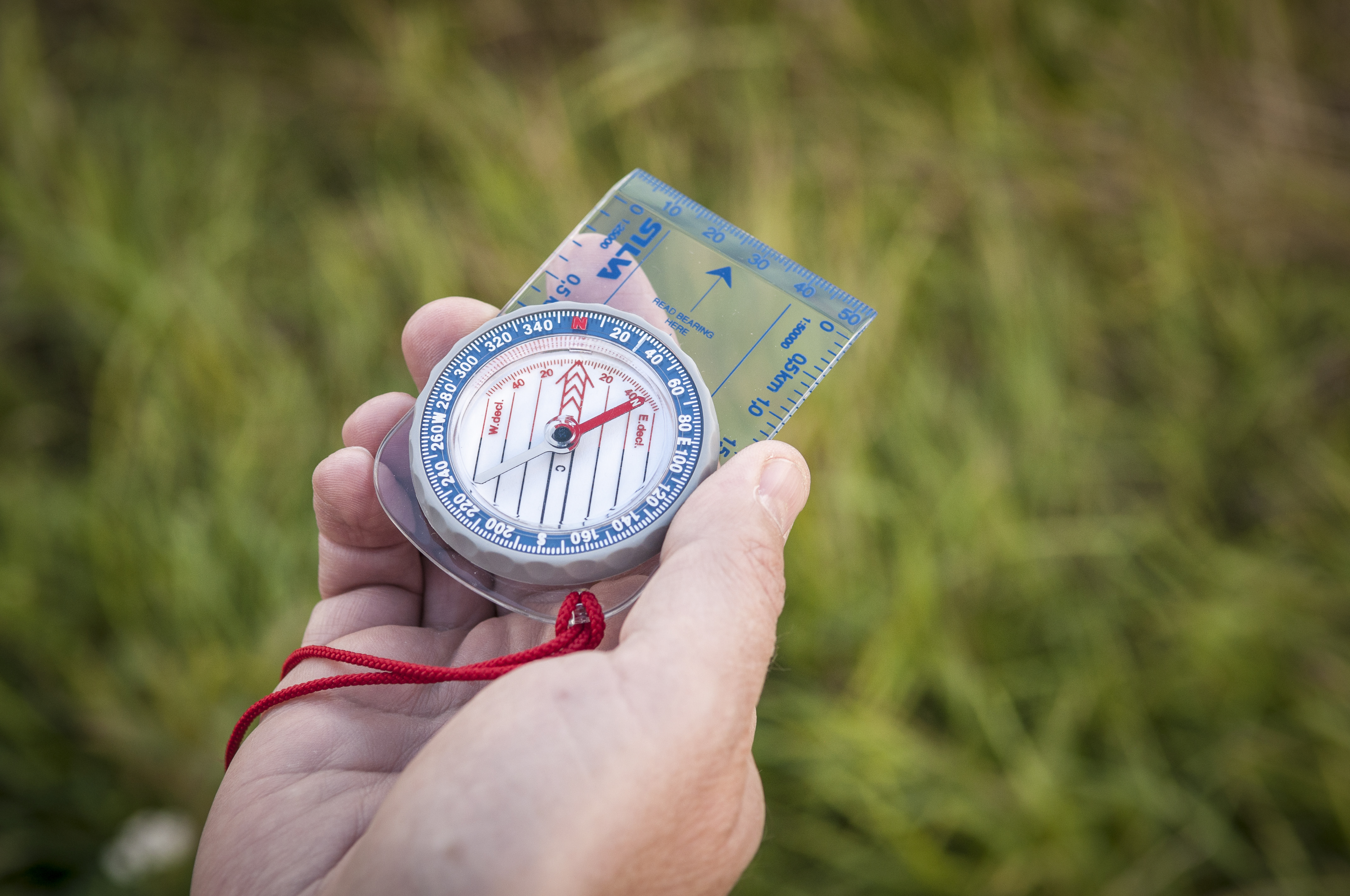 Någon står utomhus i gräset med en kompass i handen.